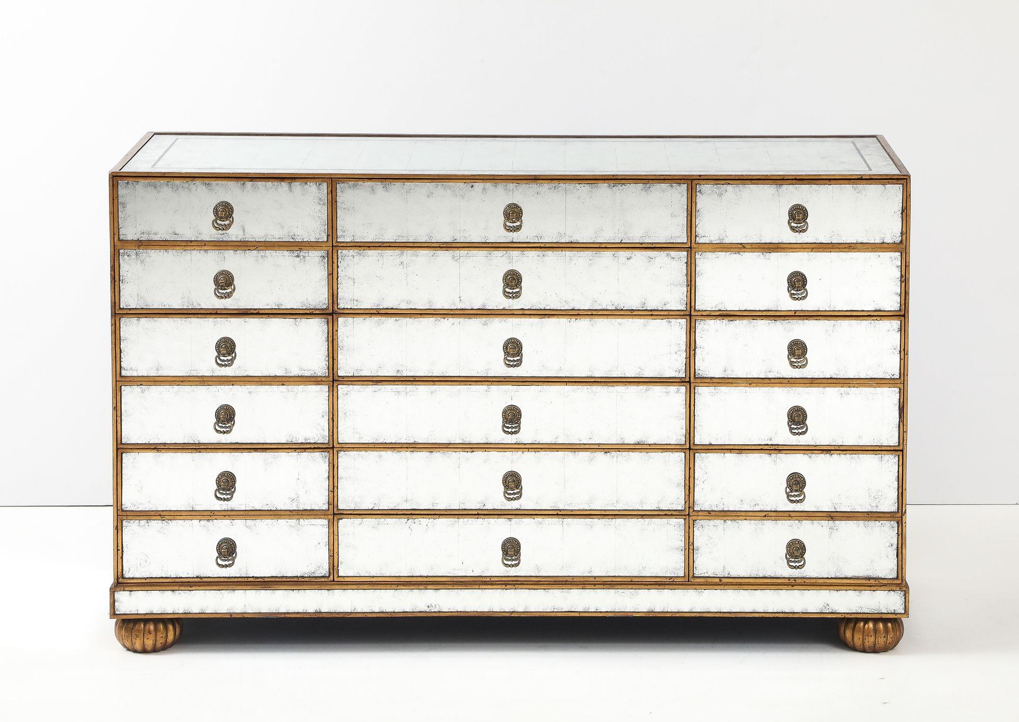 This elegant mirrored chest is a stunning piece that combines classic design with modern glamor. Featuring a distressed, antique finish on all mirrored surfaces, it has a rich, timeworn patina that adds character and depth. The gold-toned trim and