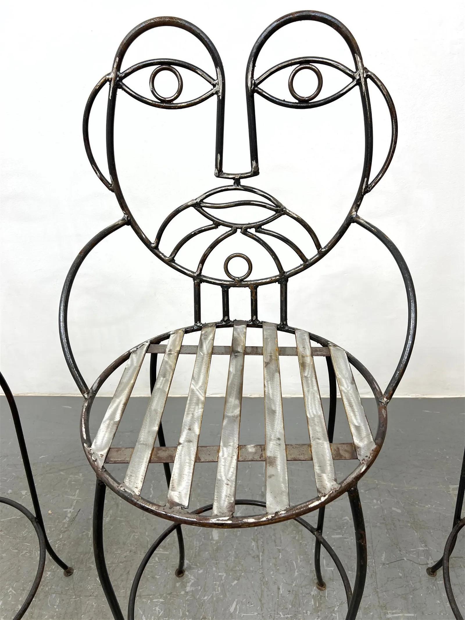 A set of 4 wrought iron barstools with round metal seats and figurative backs in the shape of a face.
