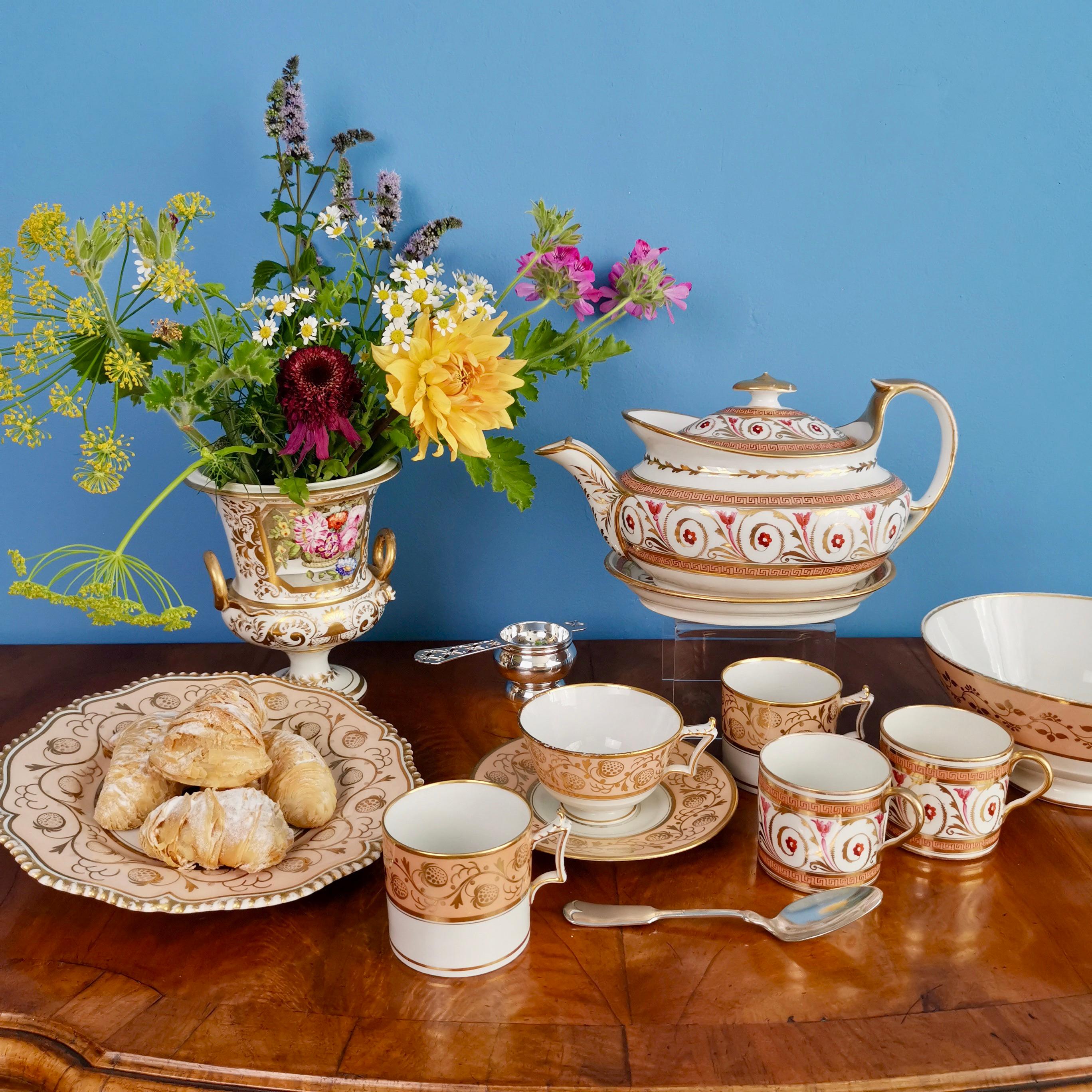 This is a stunning teapot on a stand made by John Rose at Coalport in circa 1810, which was the beginning of the Regency style. The teapot is is made in a low oval shape and is decorated with a graceful Regency-style pattern in peach, gilt and