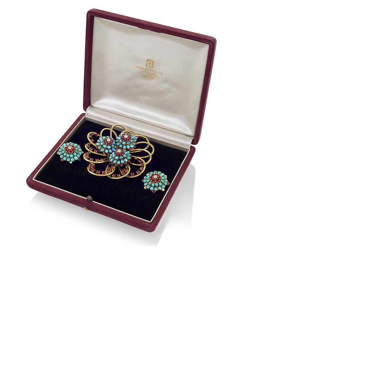 An American mid-20th century 18 karat gold brooch and earrings suite with rubies, diamonds and turquoise by John Rubel. The brooch is an openwork bloom comprised of large gold loops studded with accenting rubies that expertly play with the negative