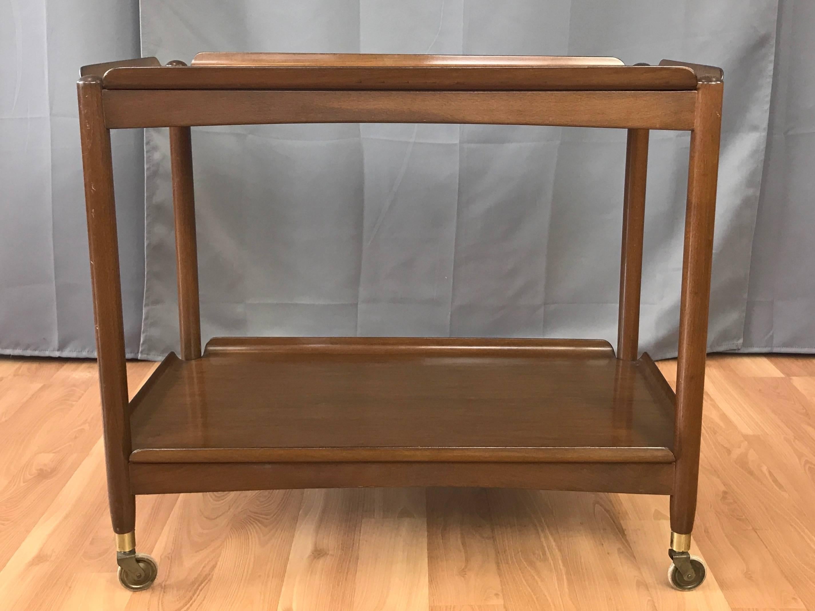 Chariot de bar ou de service pliant danois des années 1950:: avec plateaux amovibles en bois courbé:: du designer américain John Stuart. 

Le cadre en hêtre massif:: avec sa finition marron chaud:: est doté de charnières en laiton qui permettent de