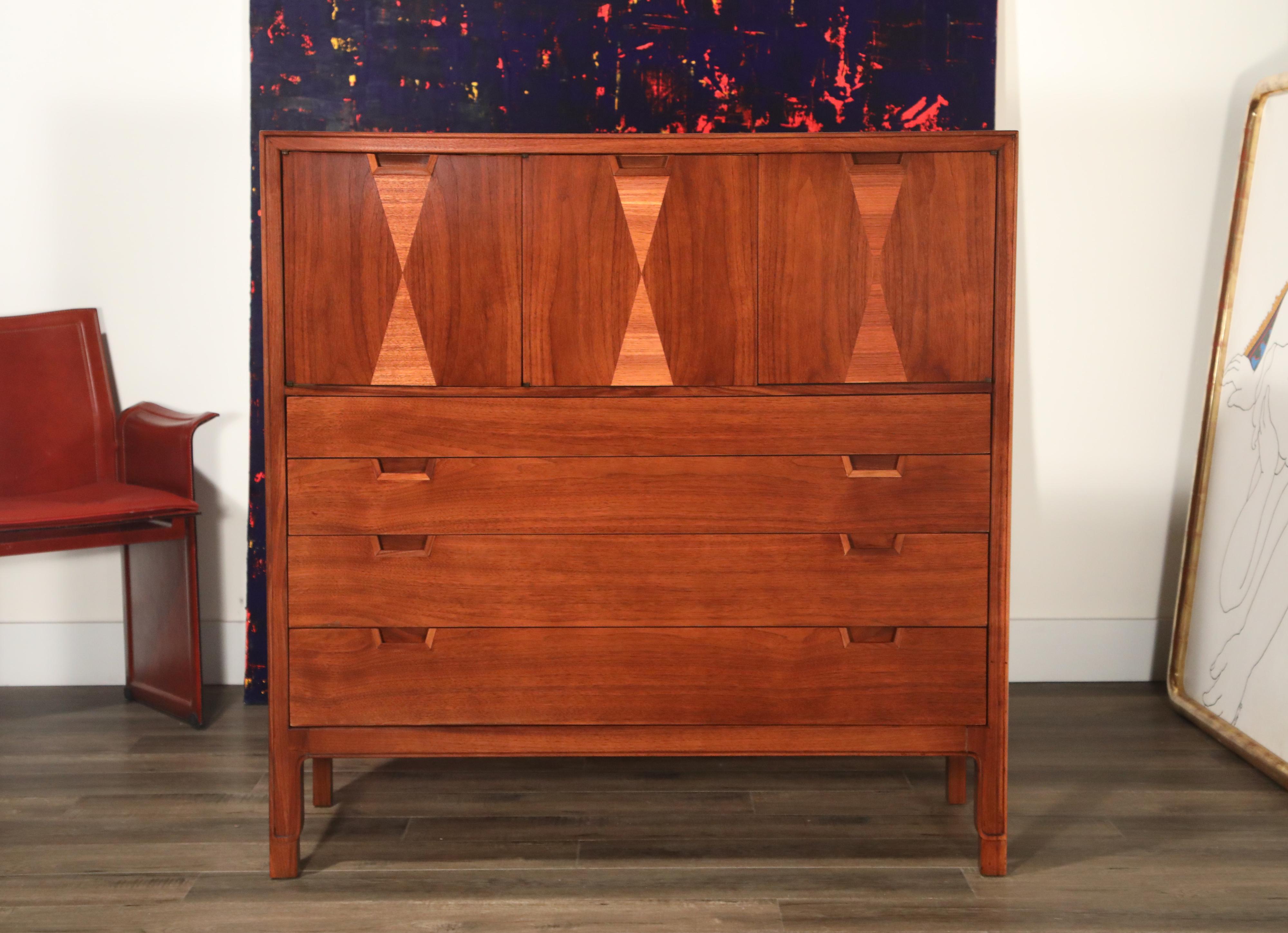 A beautifully restored highboy dresser by John Stuart for Janus Collection by Mount Airy Furniture Company. This classic 1960s design is accented by hourglass shaped alternating veneers. Cabinet doors atop open to cubby space while four drawers open