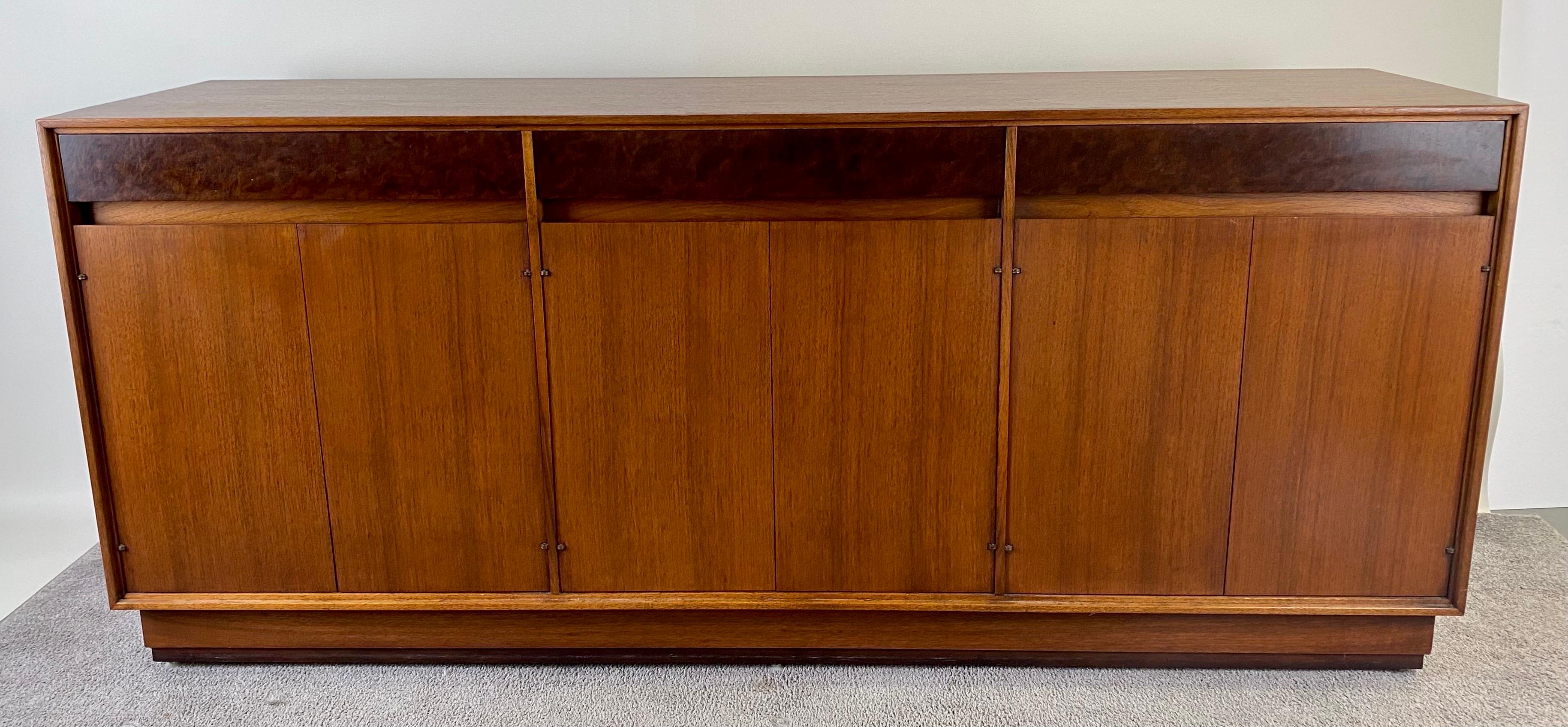 

A timeless John Stuart Mid-Century Modern Walnut and Burl Wood Sideboard Credenza. Designed by the MCM icon John Stuart , the sideboard is finely crafted by the renowned Mount  Airy Chair Company. The quality credenza features three drawer fronts