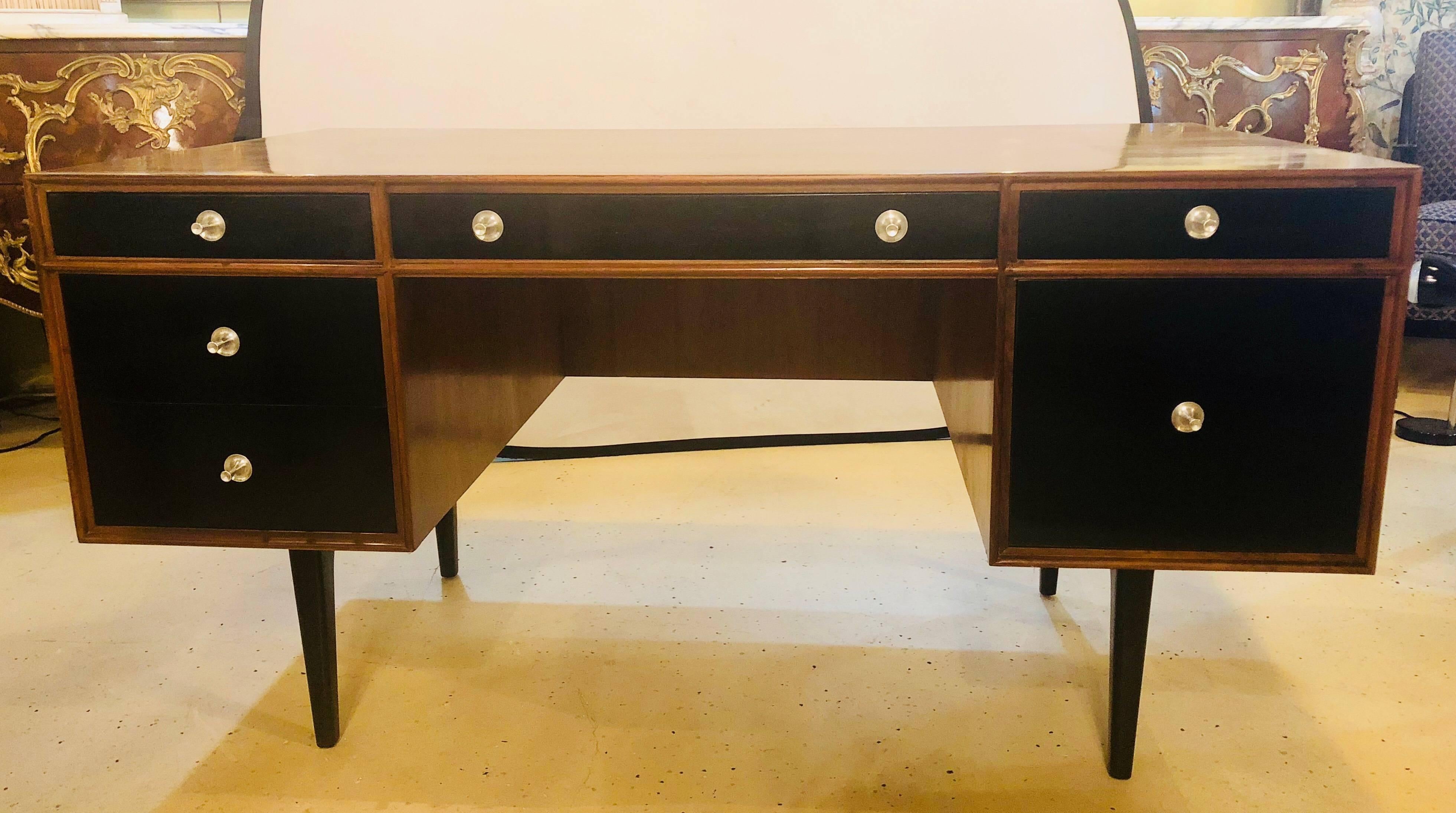 A fine custom quality desk or vanity in the manner of John Stuart. The teak finish polished and darkened to a rosewood look having ebony drawer fronts and legs. The drawers with steel polished pulls have three up top with two side by one file