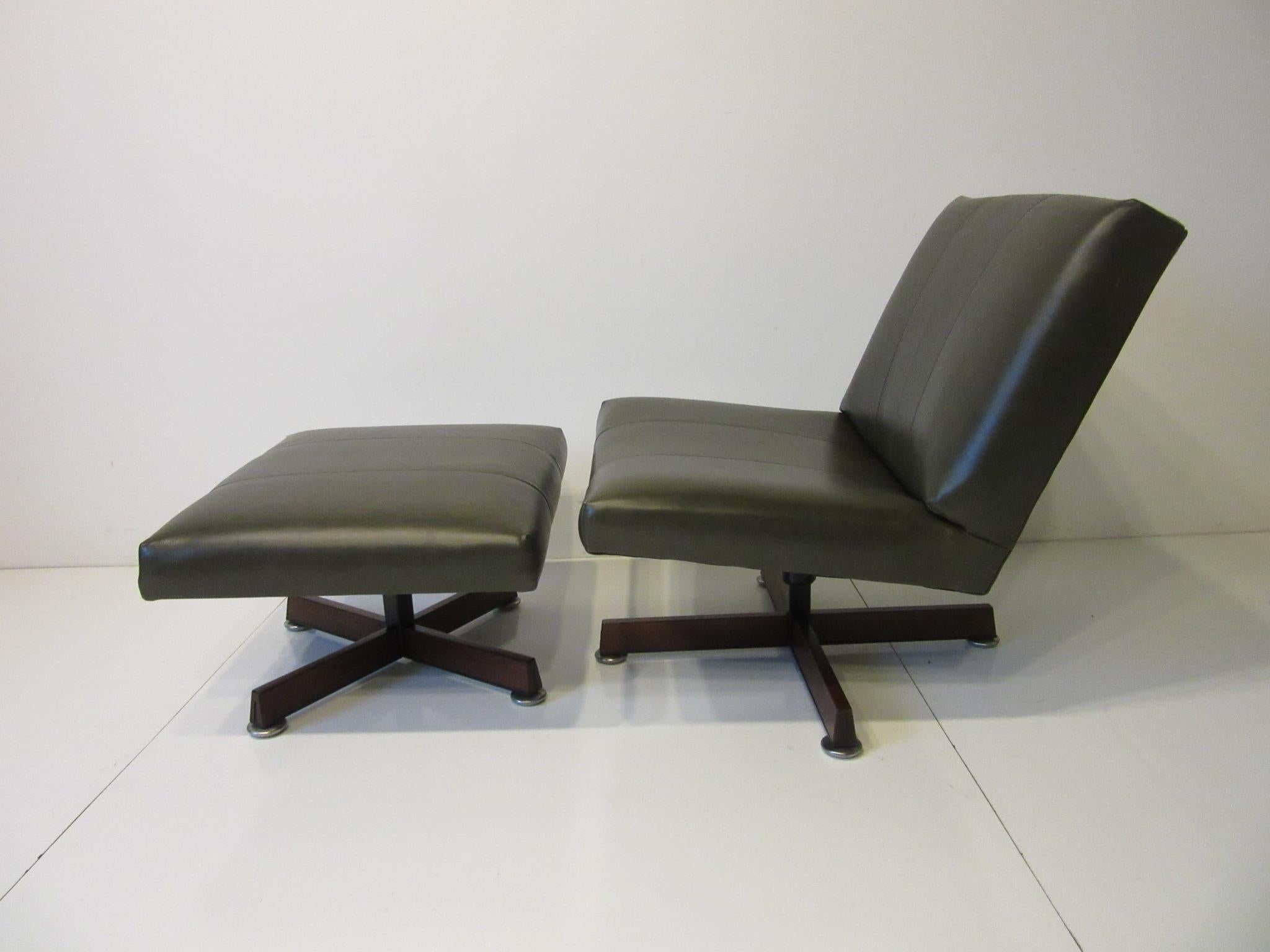 A olive green leather swiveling armless lounge chair and swiveling ottoman with dark walnut star bases by John Stuart for his Hastings Square Collection. Retains the paper label this well crafted, simple, comfortable set goes with any type of