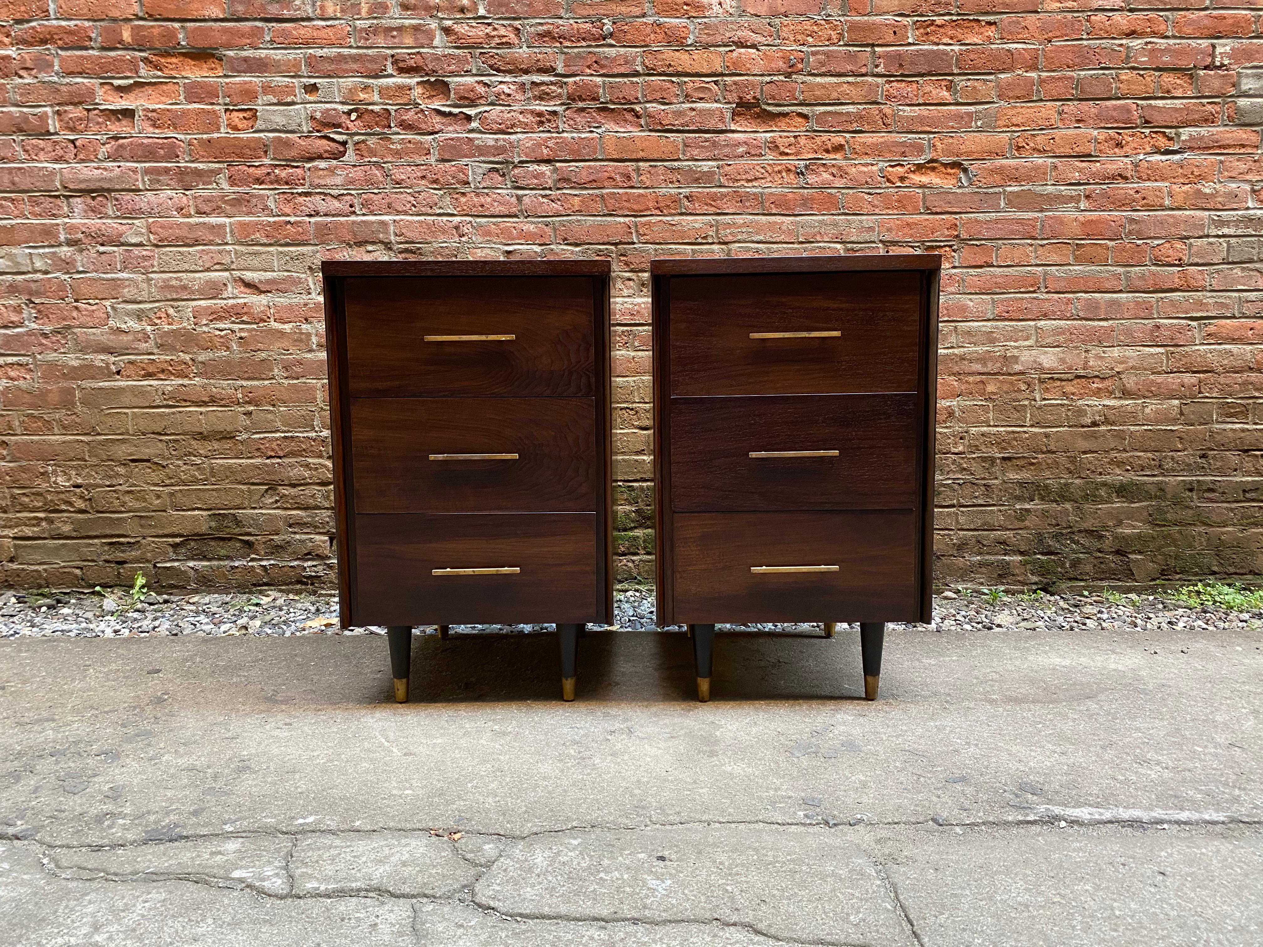 A pair of walnut and brass three drawer end tables for John Stuart, circa 1960. Refined in their simplicity. Good condition with some minor veneer losses and tarnish to the solid brass hardware. One John Stuart enamel button