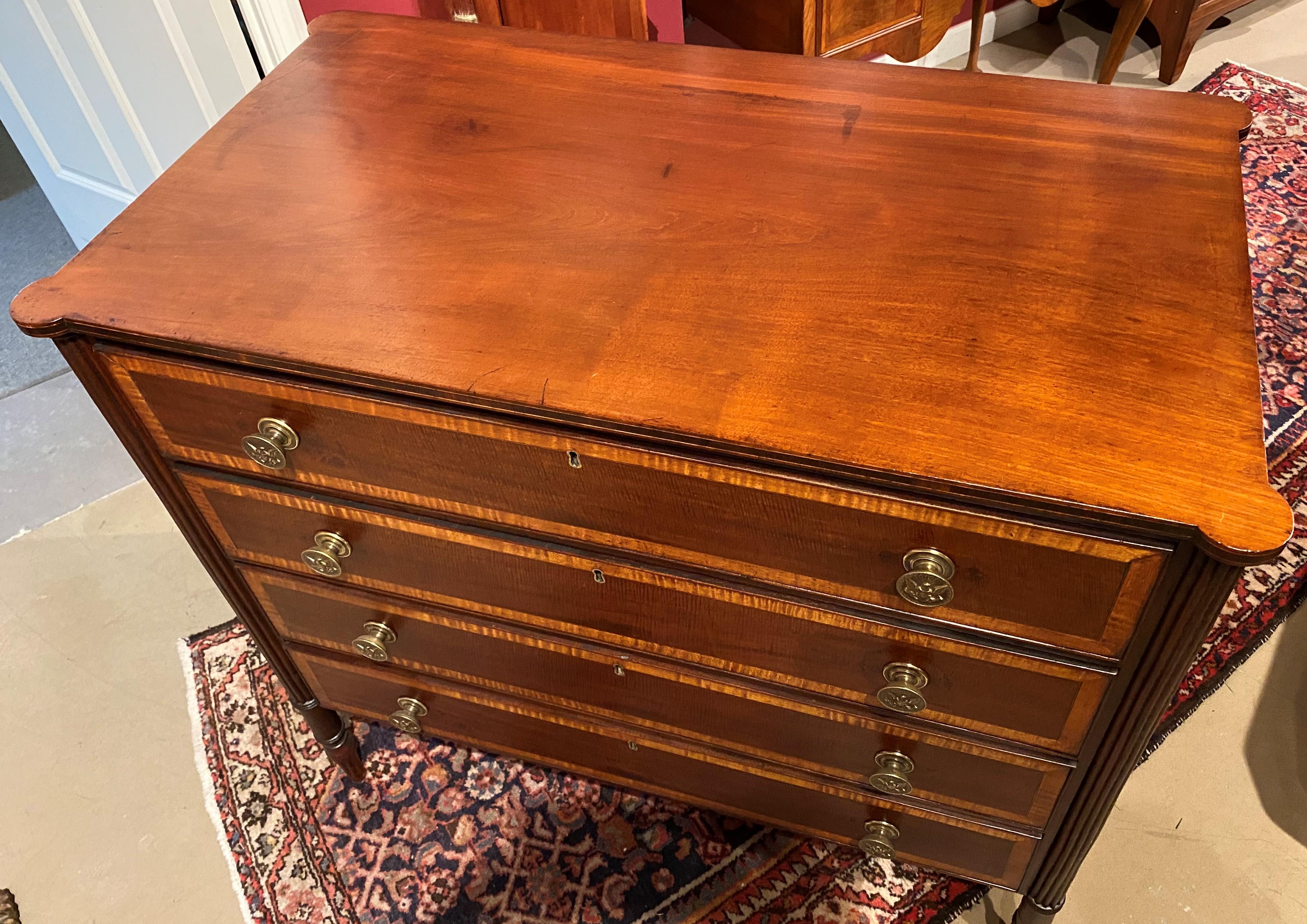 A fine Seymour School four-drawer rectangular chest in mahogany with a conforming top featuring turret corners and line inlay, surmounting a four-drawer case with fine banded drawer fronts with cockbeading, punched eagle decorated brass pulls,