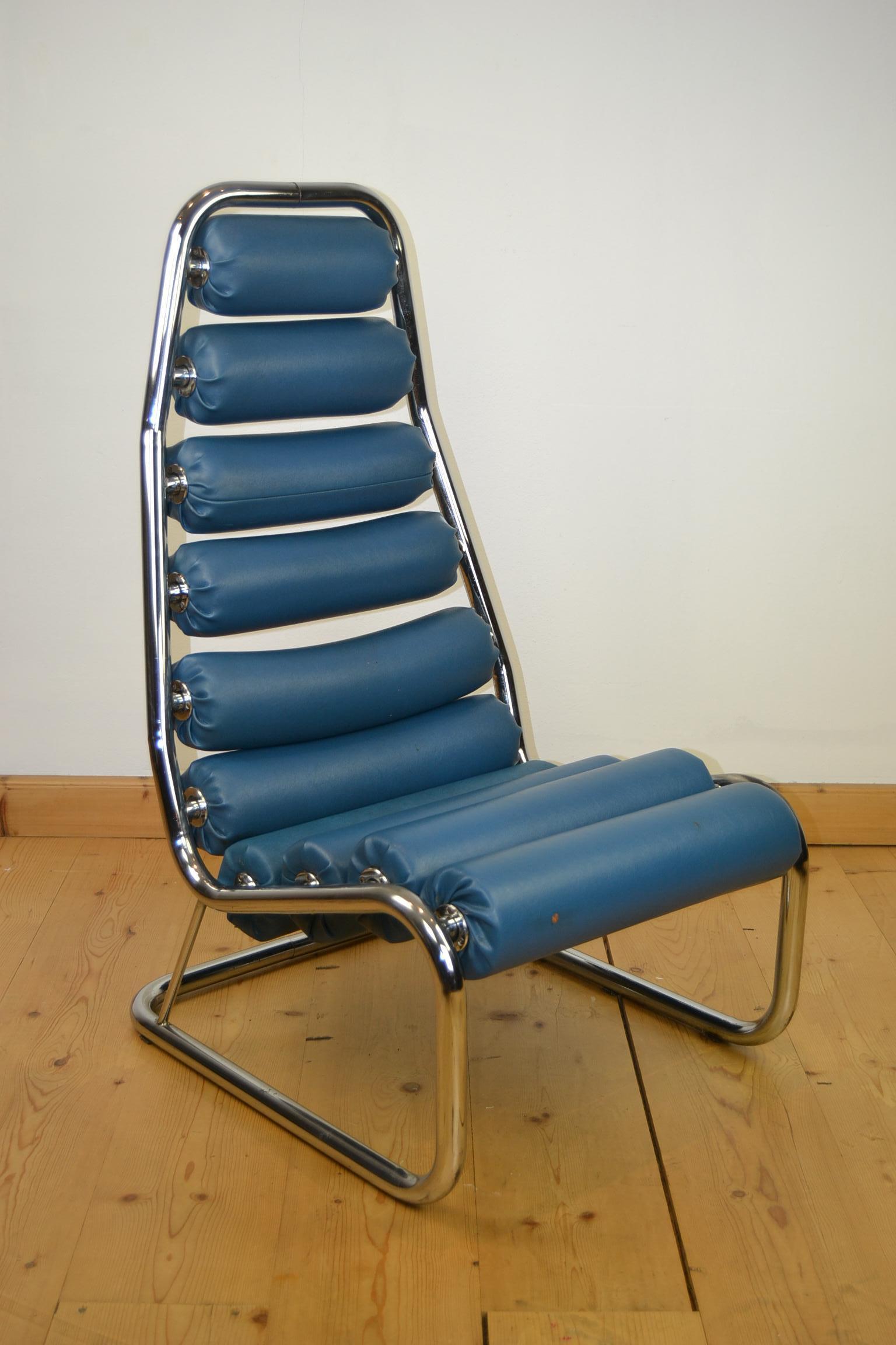 Blauer Clubsessel aus den 1970er Jahren. 
Ein auffälliger Stuhl aus einem verchromten Gestell mit 10 blauen Kunstlederrollen, die sich drehen lassen. Diese Rollen bringen Sie auch im Fitnessstudio zum Nachdenken. 

Dieser Sessel mit Rollen wurde