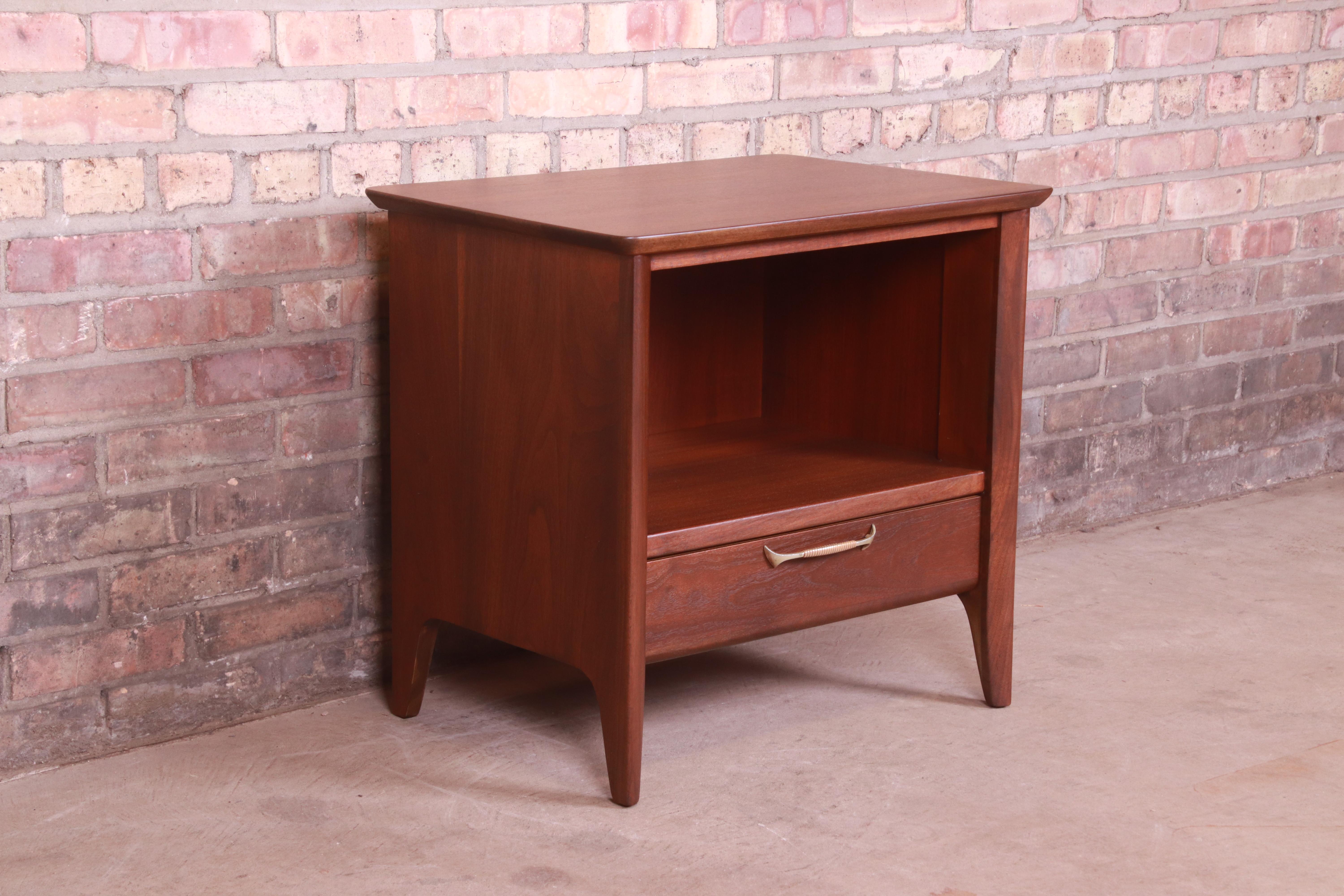 A stunning Mid-Century Modern nightstand

In the manner of John Van Koert for Drexel

USA, 1960s

Sculpted walnut, with original brass hardware.

Measures: 24