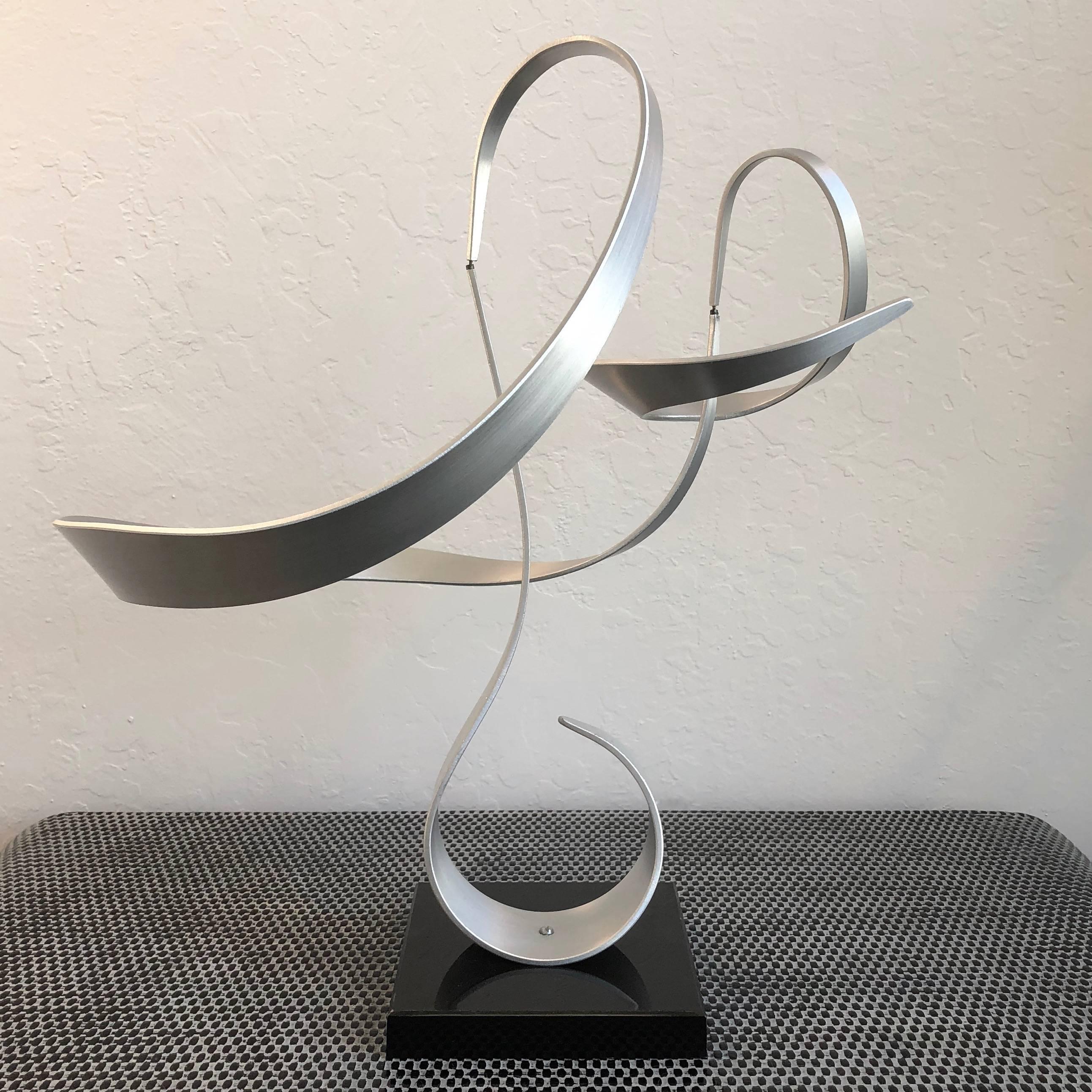 A mesmerizing abstract kinetic sculpture by 1970s artist John W. Anderson.

Comprised of three gracefully twisting brushed aluminium ribbons on a black acrylic base. The top two segments balance weightlessly on tiny pins, allowing them to