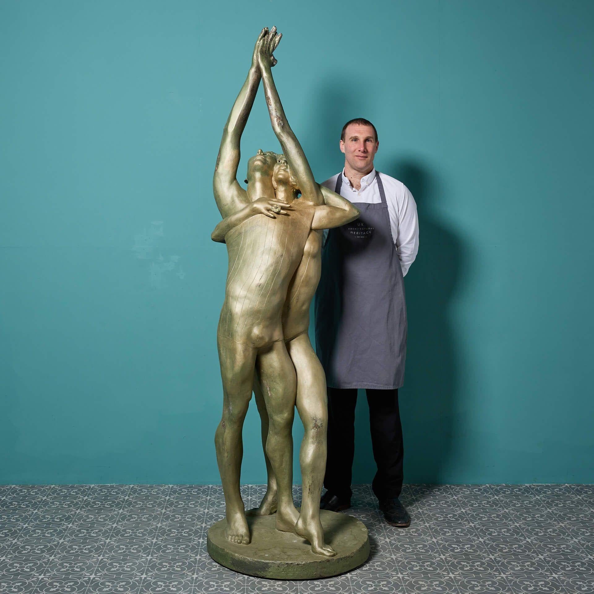 A large patinated resin sculpture titled ‘Dancers - arms raised’ by the acclaimed British sculptor, John W Mills.

In an impressive scale and eye catching patinated gold lustre finish, this life-size figurative sculpture depicts male and female