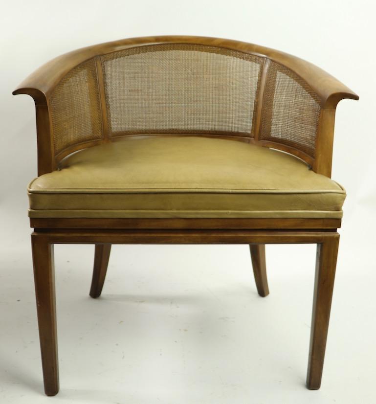 Stylish and chic barrel back lounge chair by John Widdicomb. Solid wood frame, with caned sides and backrest, leather upholstered seat. This chair is in clean, original and ready to use condition. Second chair available but as is. not included in