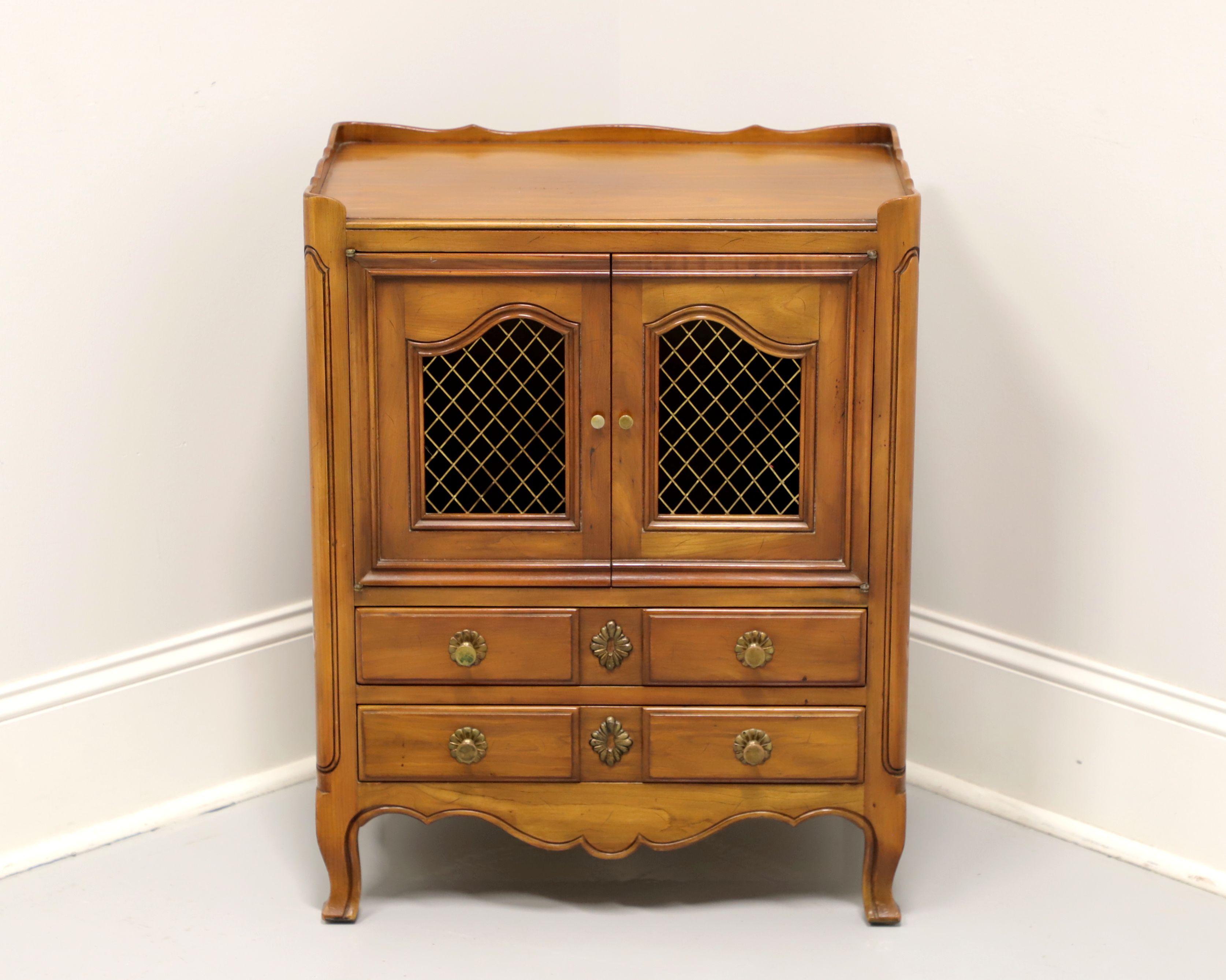 A French Country style nighstand by John Widdicomb, of Grand Rapids, Michigan, USA. Solid cherry with brass hardware, carved gallery to top, brass screens to door fronts, carved panels to front sides, curved legs and scroll feet. Features upper
