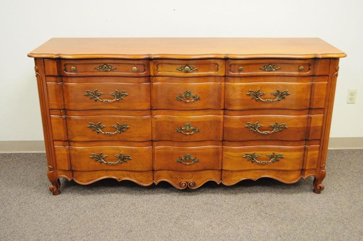 John Widdicomb Country French or Provincial solid cherry dresser. Item features solid cheerywood (or fruitwood) construction, 12 dovetail constructed drawers, ornate solid brass hardware, carved sides, shaped top, working locks and original John