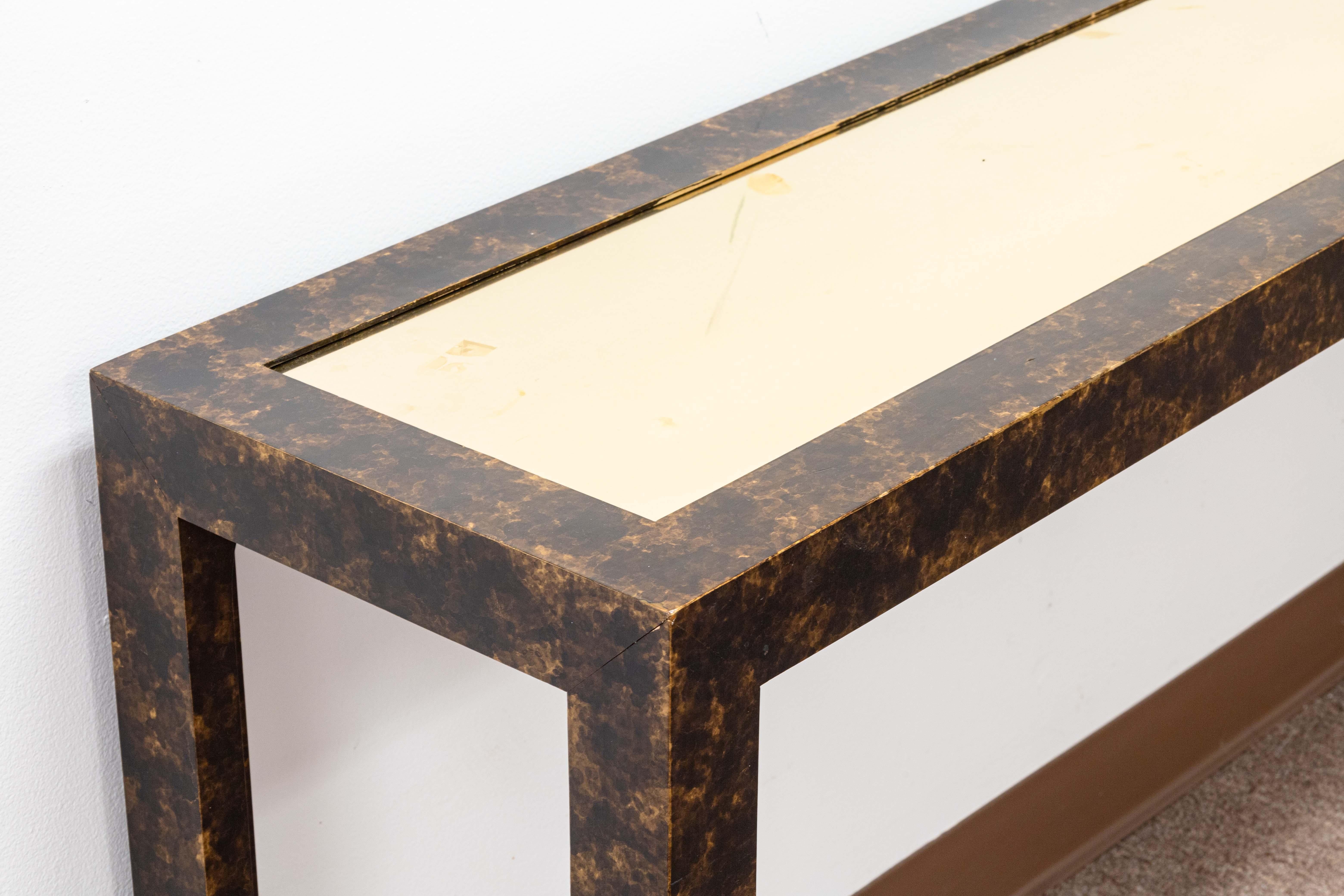 A John Widdicomb parson console table. This pretty console table features a wood construction with a semi-glossy faux tortoise shell finish. This piece has a brass table top in the center. The Widdicomb tagging can be found on the underside of the