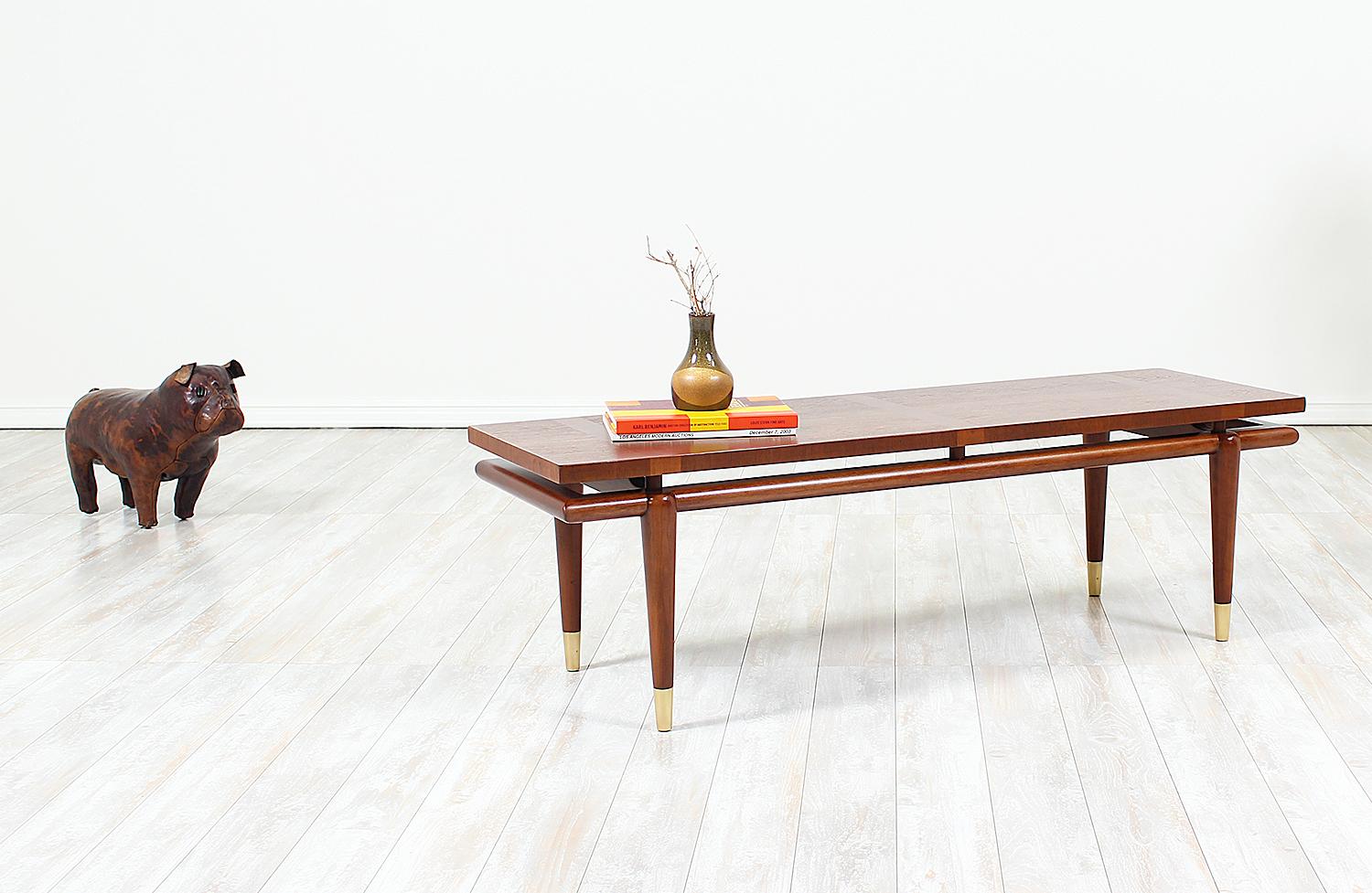 Unique mid-century coffee table designed by John Widdicomb and manufactured by John Widdicomb Co. in the United States circa 1950s. Elegantly crafted in walnut wood, this coffee table features tapered legs that are capped at the feet with brass