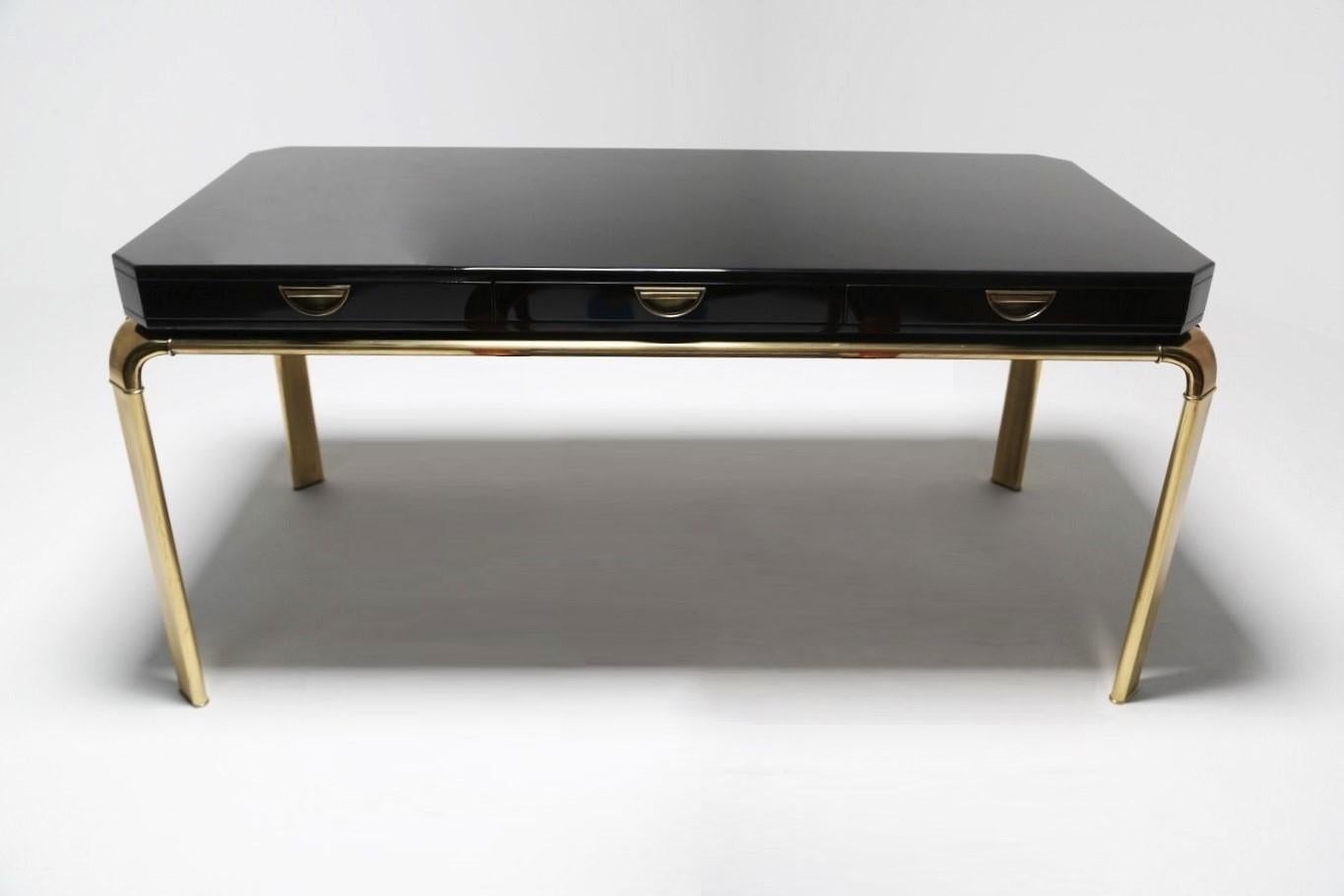 This Classic writing table or desk by John Widdicomb for Mastercraft. Composed of a large black lacquered wood top with canted corners that sits atop a brass frame. Brass legs swoop outwards and evoke the graceful line of a waterfall. Recessed