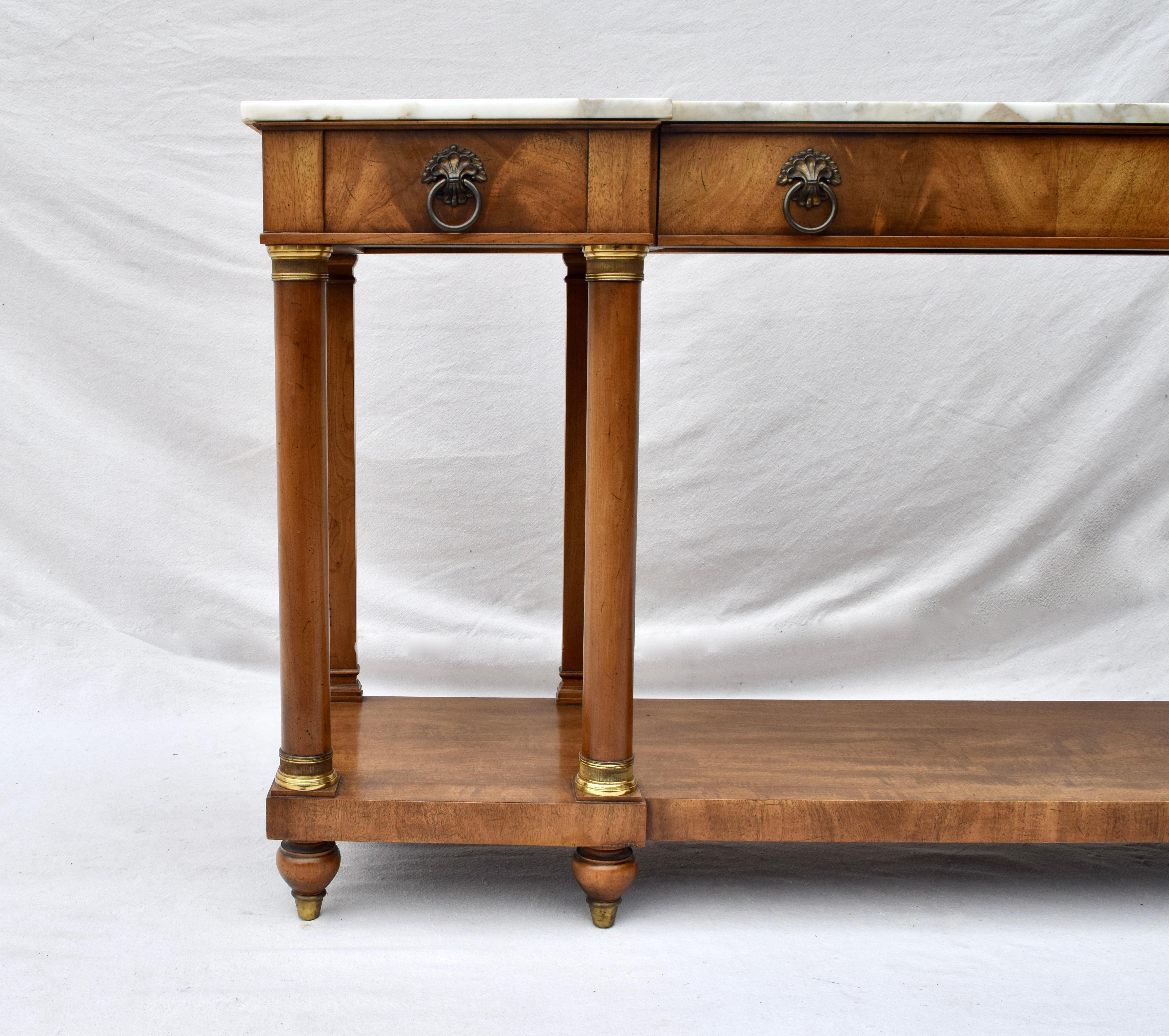 A two tier French Neoclassical style console table or sideboard made by William Berkey Furniture for John Widdicomb. Italian marble top conforms to the eight column brass embellished base with three storage drawers & turned, tapered brass capped bun