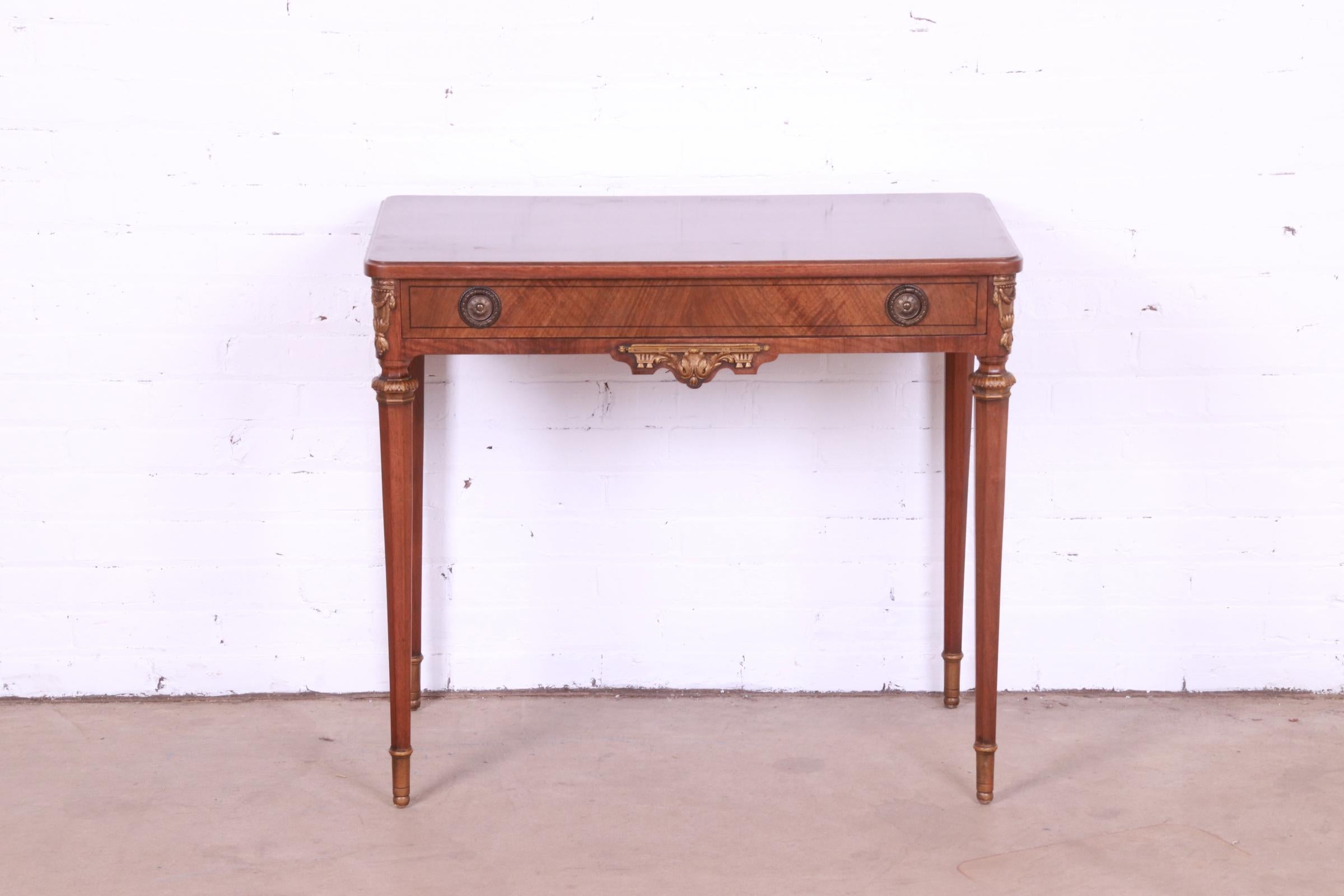 A gorgeous French Regency Louis XVI style vanity or writing desk

By John Widdicomb.

USA, Circa 1920s.

Inlaid walnut, with carved giltwood details, and original brass hardware.

Measures: 33