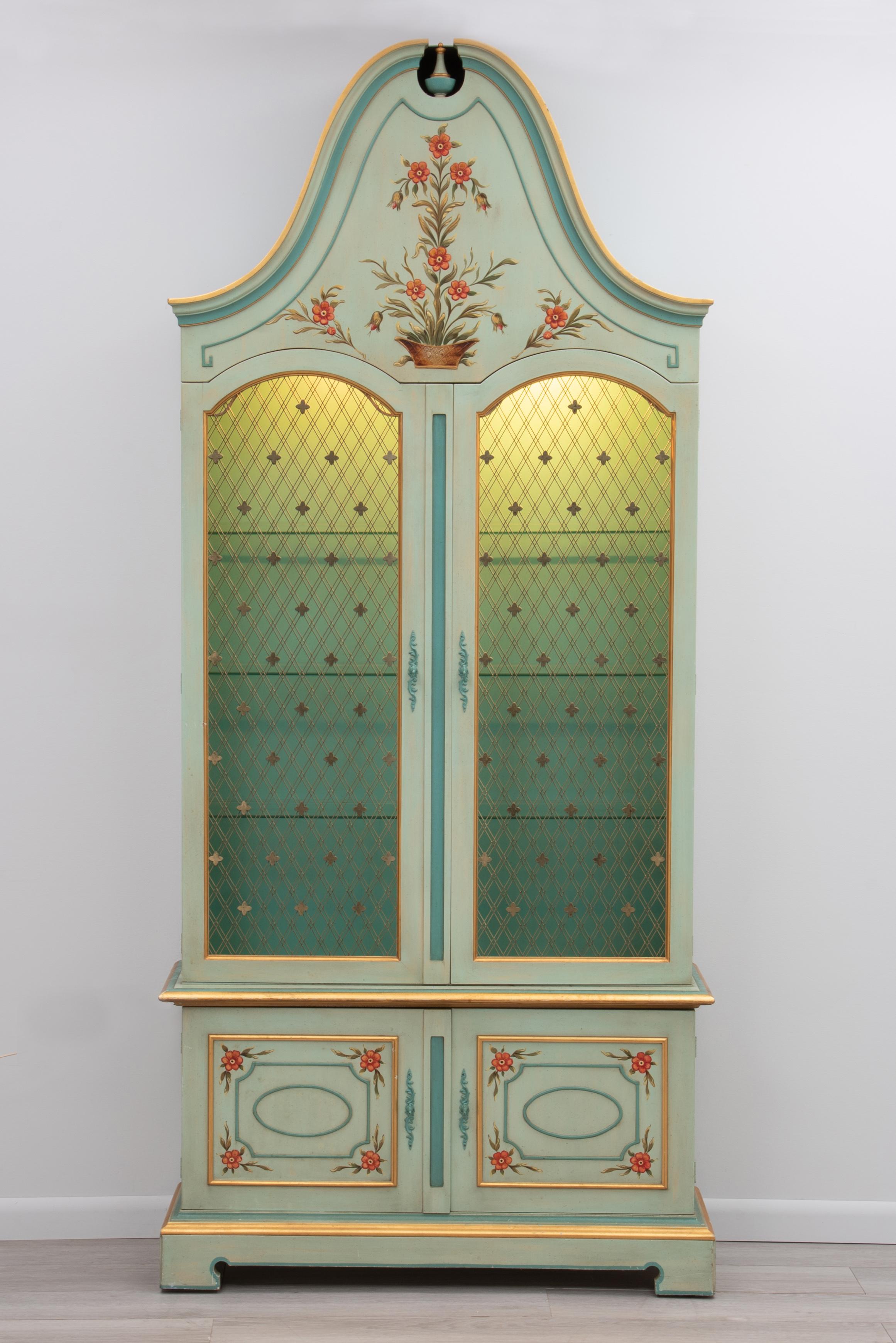 A beautiful two piece paint decorated two door cabinet by John Widdicomb of Grand Rapids, Michigan. The cabinet features wonderful hand painted decoration on the front and sides, gold leaf, large scale bonnet top, brass lattice on the doors, bracket