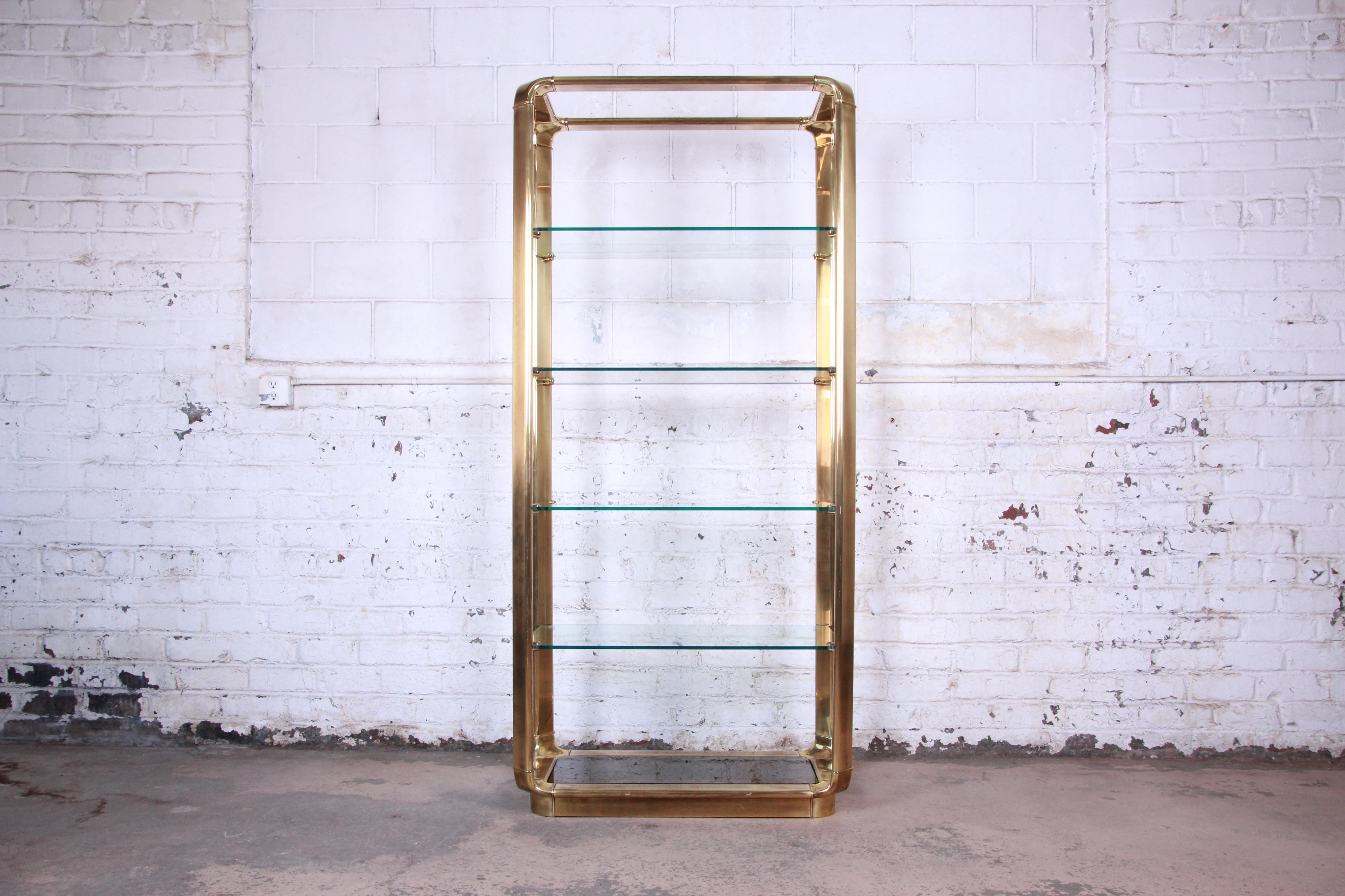 Offering an exceptional Mid-Century Modern Hollywood Regency brass and glass étagère by John Widdicomb of Grand Rapids. The étagère features a heavy solid brass frame with waterfall corners. It has four thick glass shelves with canted corners, and a