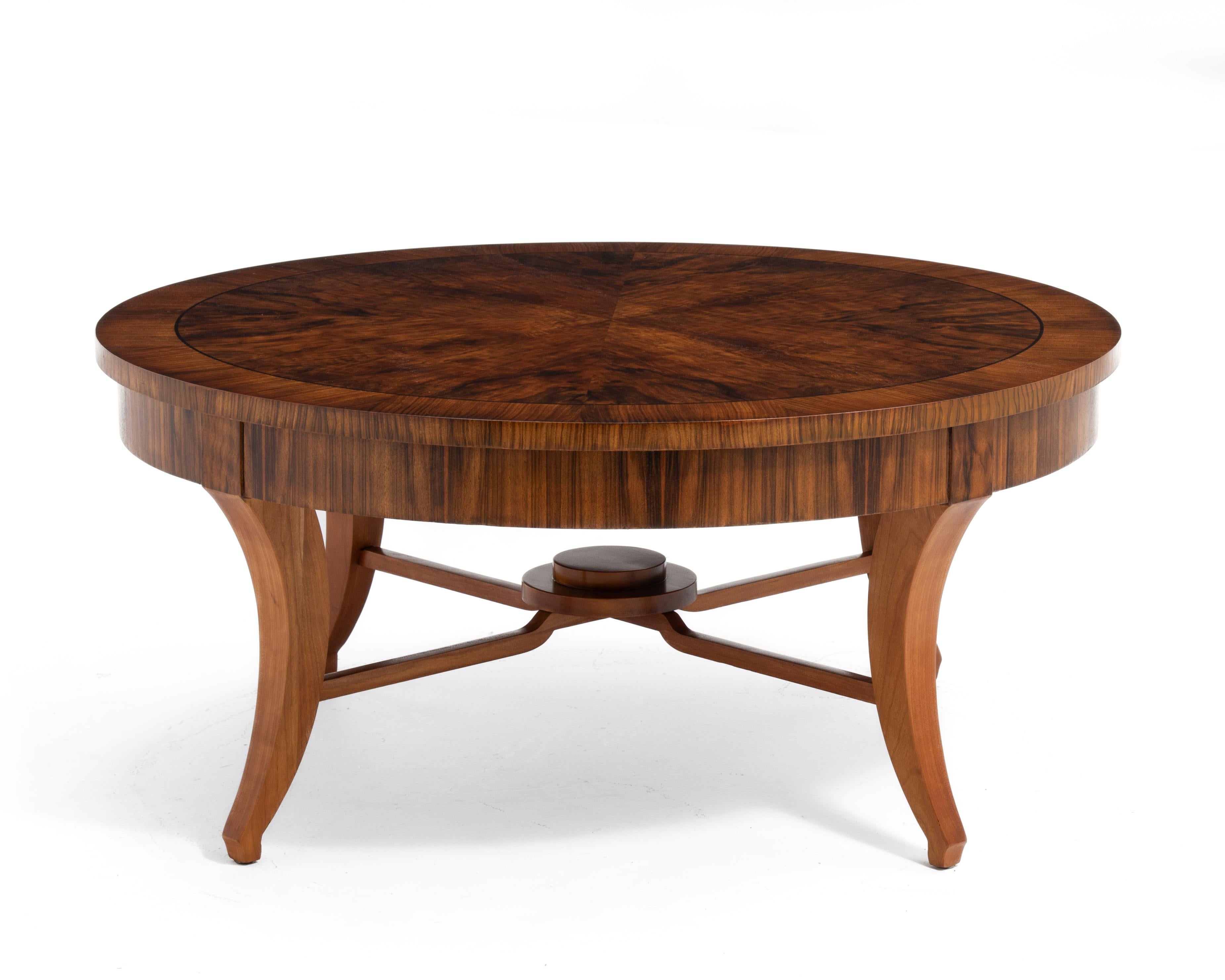 A round coffee table by John Widdicomb. The table features four book matched center panels in an exotic wood (Santos Rosewood?) with an ebony inlay and a highly figured border. The top sits on a nicely contrasting cherry base with four