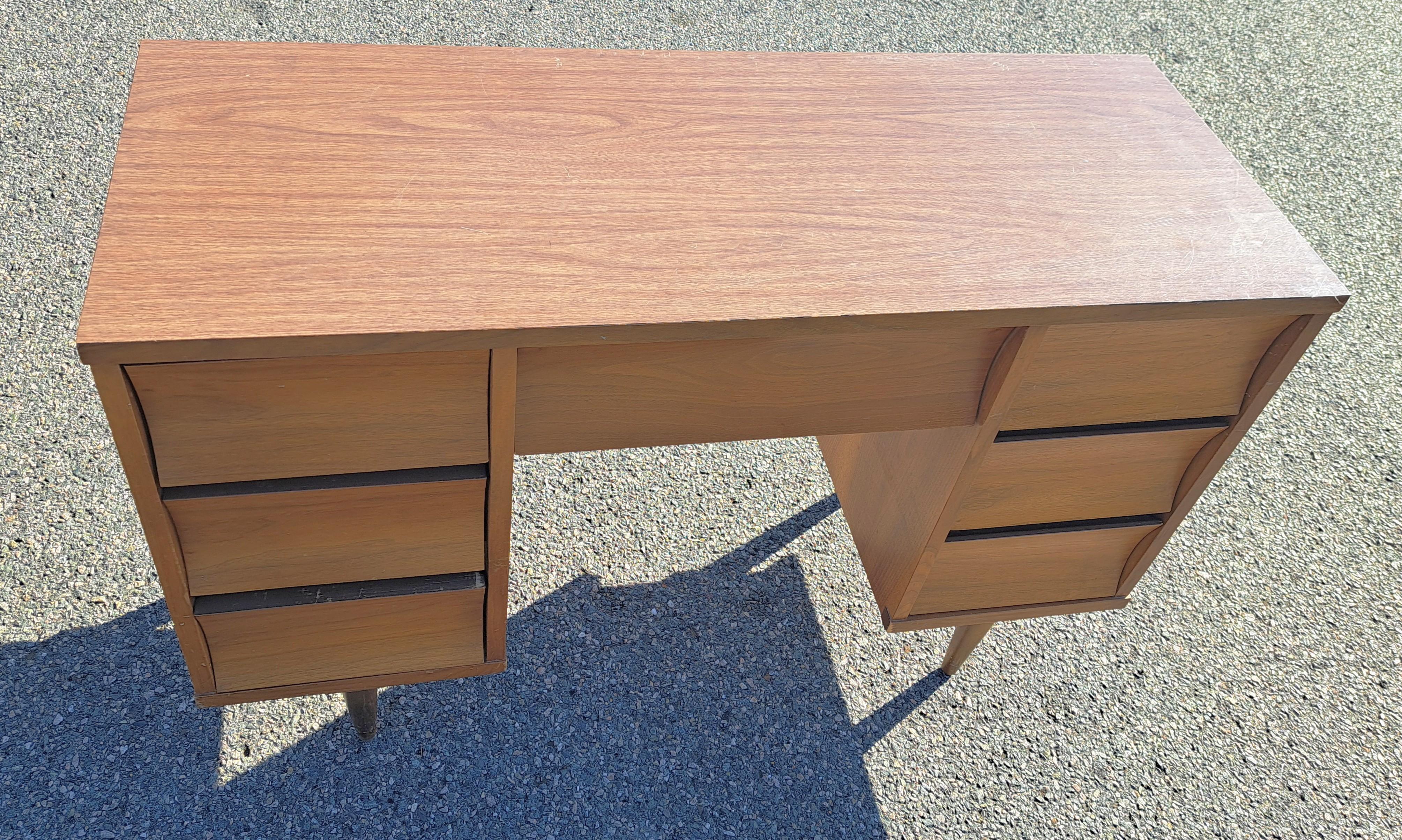 Scrivania in legno Johnson Carper Mid=Century Modern con sette cassetti frontali concavi che si estraggono facilmente senza tiranti. La scrivania ha quattro gambe a pioli e un piano in formica.