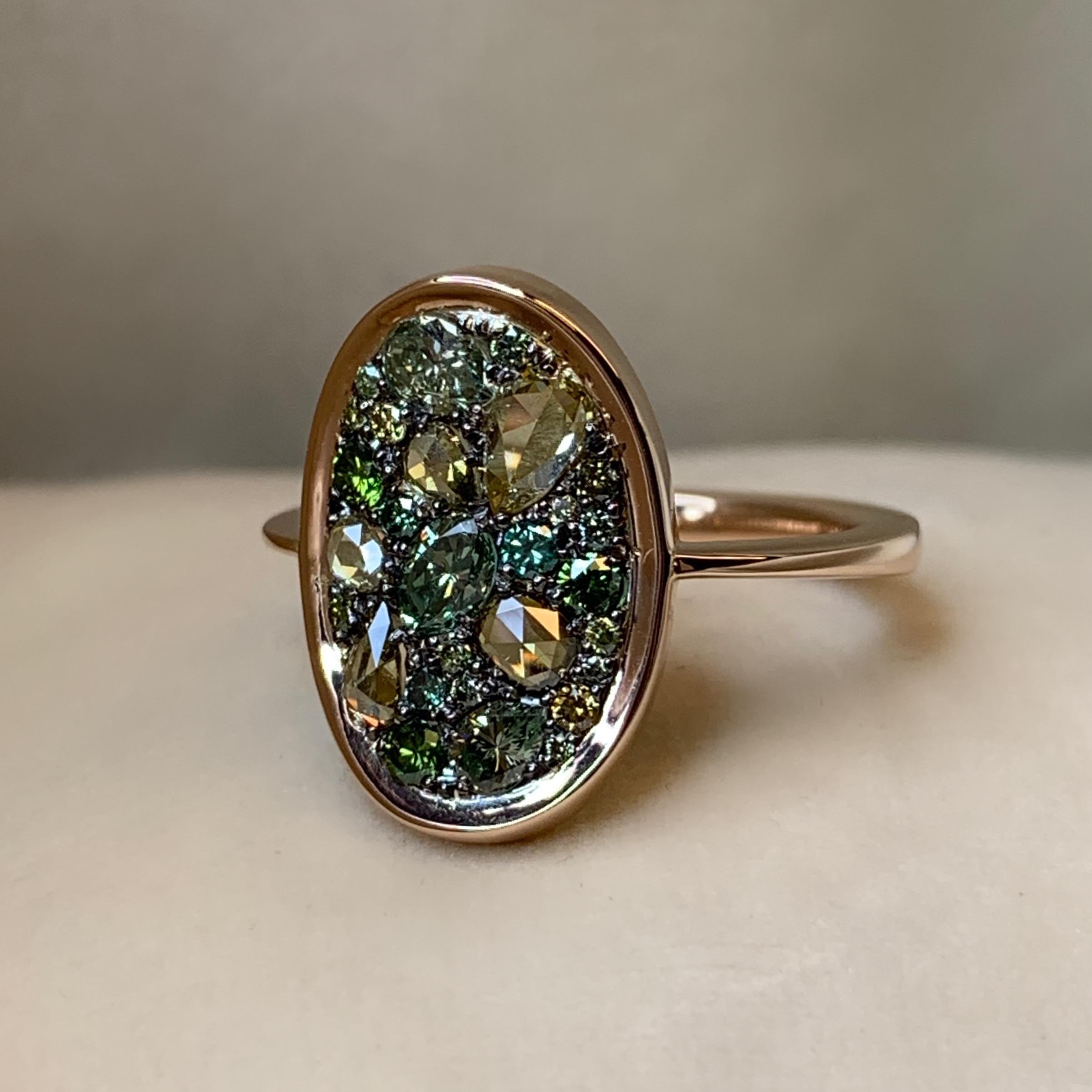 One of a kind ring in 18K Rose gold 4,7 g & blackened sterling silver (The stones are set on silver to create a black background for the stones)
Set with Fancy olive green rose-cut diamonds, fancy olive green & natural coloured green brilliant-cut