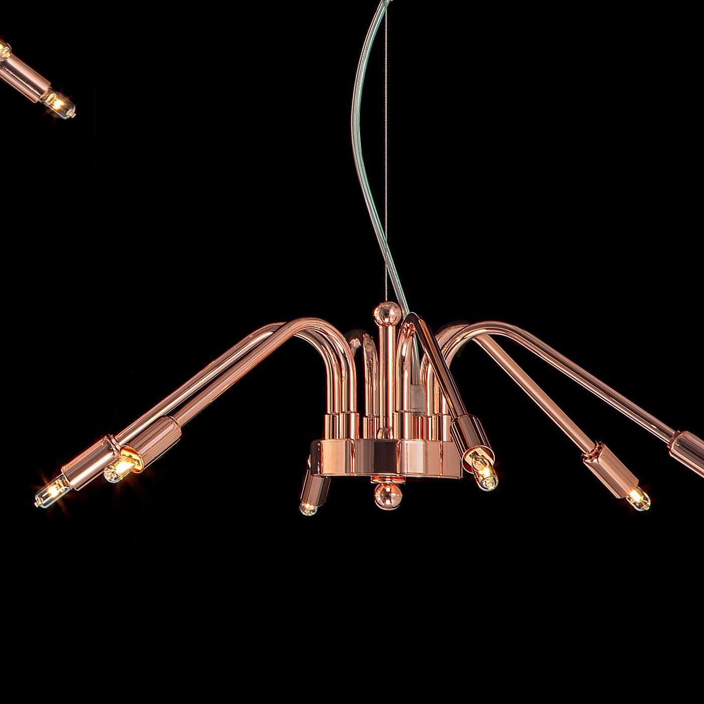 This modern chandelier features a simple yet unique design. Fixed on a metal ceiling rose, the brass and metal structure features a round-shaped central element supporting six curved and slanted arms. Boasting a polished copper finish, this stunning