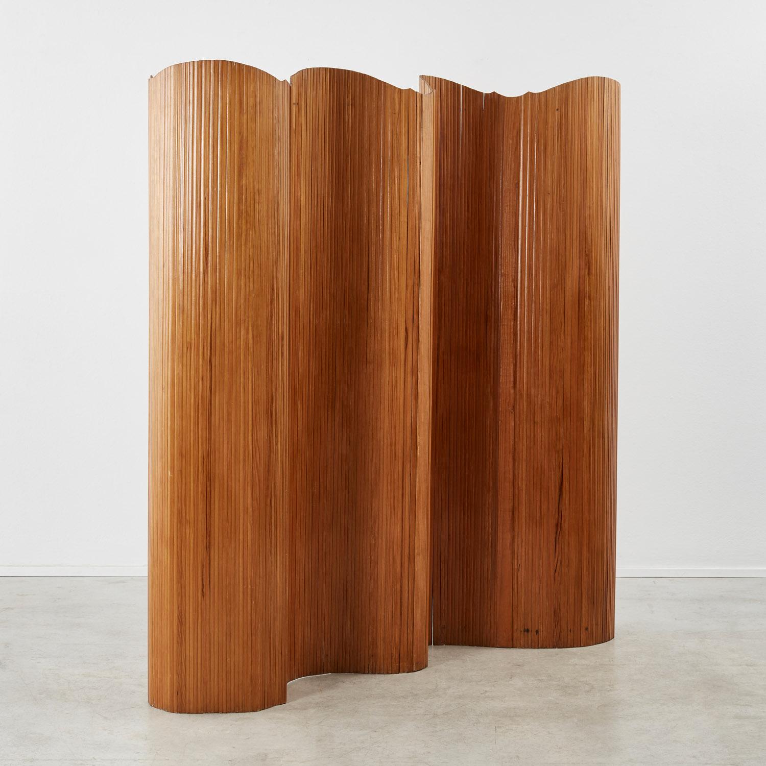 This twentieth-century screen after the design by Alvar Aalto, possibly Baumann Fils et Cie, Melun-Paris. Its pine slats are stained and polished, and the flexibility of the joints – which are capable of unfurling in several configurations – is made
