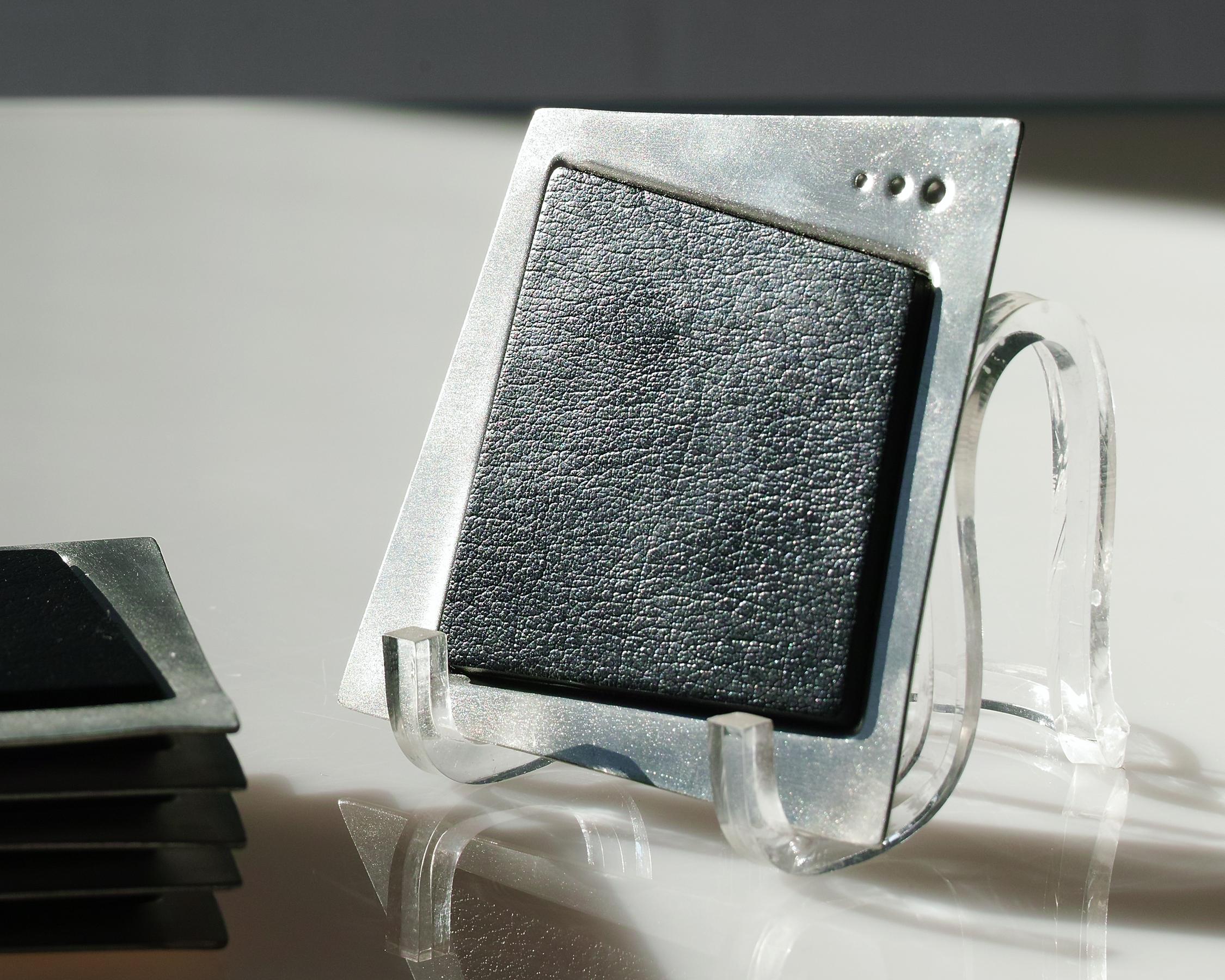 For your consideration is this set of four handmade pewter and leather coaters by metalsmith, Jon Michael Route (b. 1954). They have distinctive trapezoidal forms with inset black leather pads and three dot details to one side. A modern, elegant
