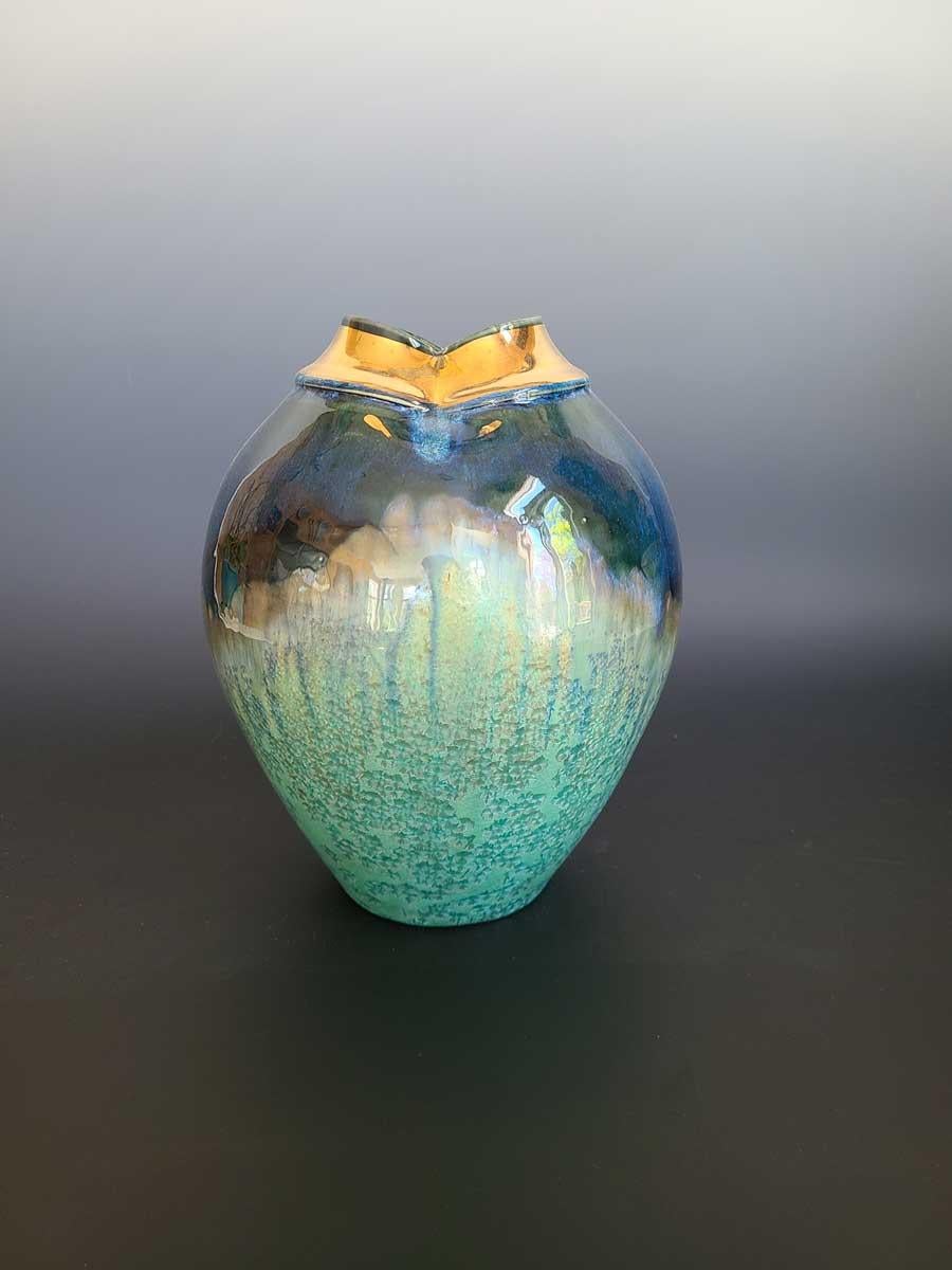 This small abstract vessel by ceramicist, Jon Puzzuoli, is made with glazed turquoise porcelain. The glaze is a combination of light teal green and deep, midnight blue, blended together around the widest part of the body which results in an almost