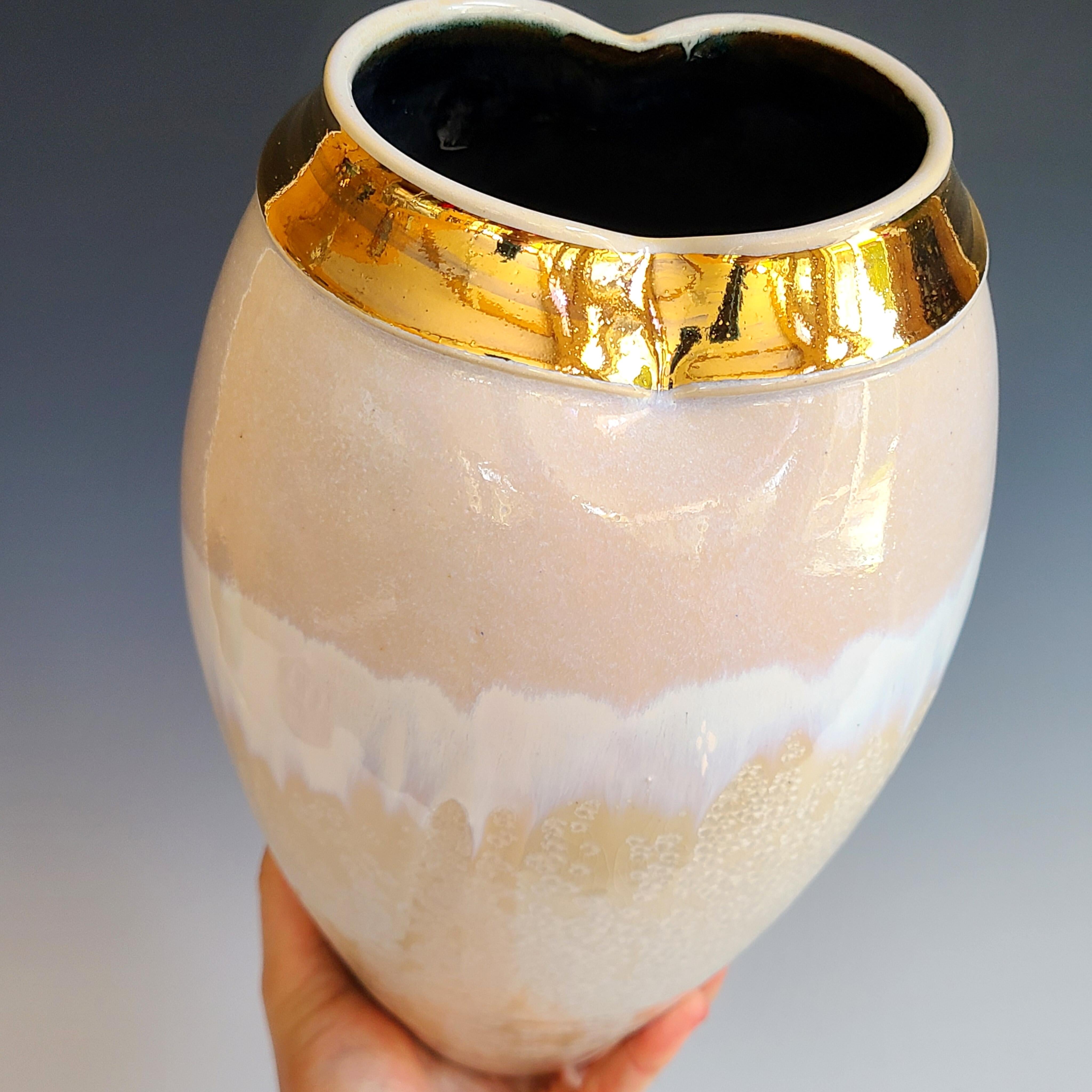 This glazed porcelain vessel by Jon Puzzuoli features a neutral, off white and white palette and a crystalline glaze over the bottom portion of the piece. It is finished with 18K gold luster on the neck. The artist's stamp is located at the base of