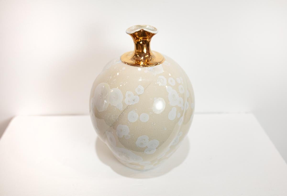 Questo vaso in porcellana smaltata cristallina di Jon Puzzuoli presenta una tavolozza di colori bianchi e crema con un collo stretto e un labbro rifinito in oro 18 carati. 

Gli smalti cristallini sono speciali smalti ceramici in cui i cristalli di