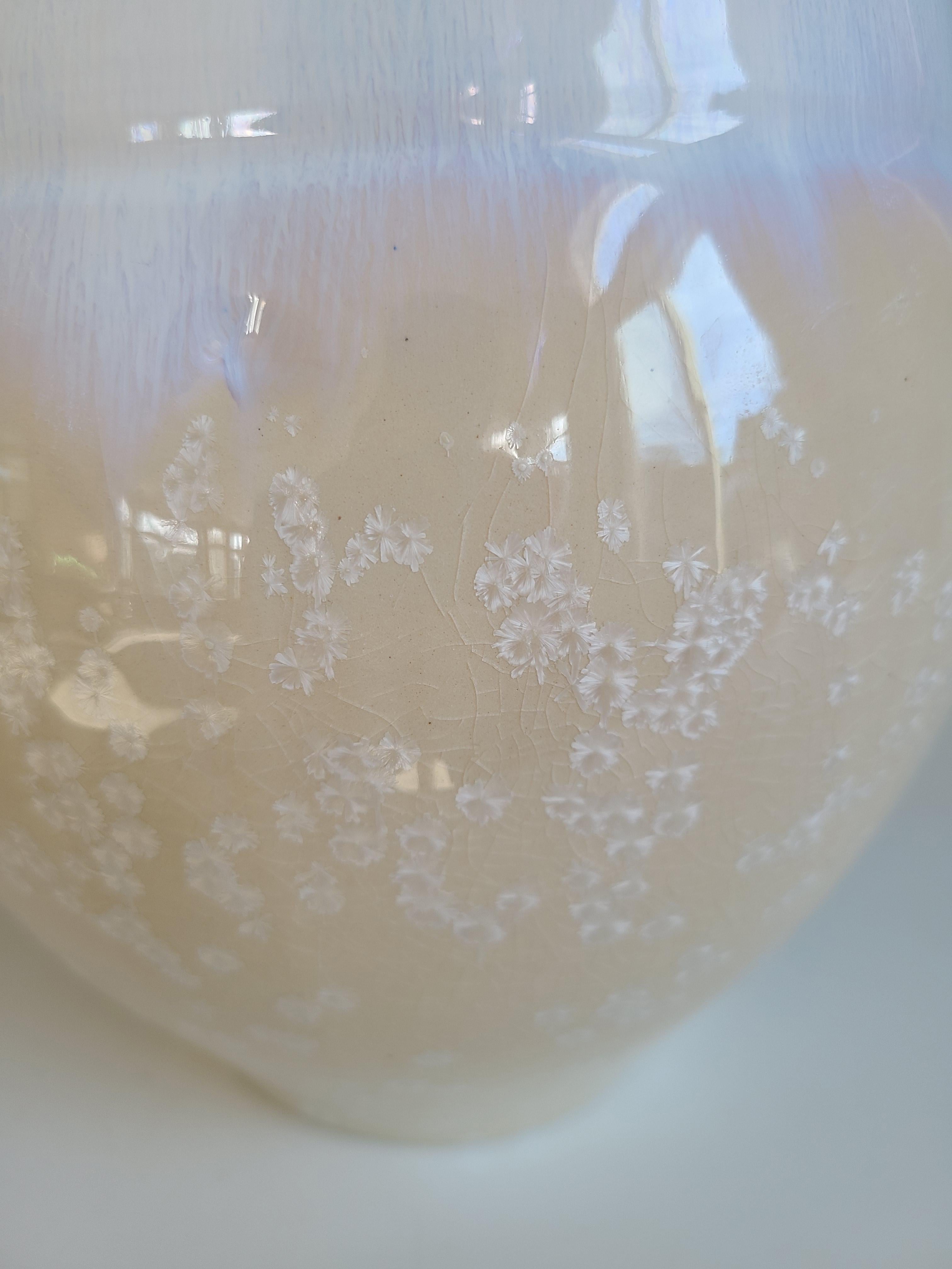 Dieses Keramikgefäß von Jon Puzzuoli ist aus Porzellan und einer kristallinen Glasur gefertigt. Es zeichnet sich durch eine helle, neutrale Farbpalette aus Creme, Weiß und Gold aus. Der untere Teil des runden, gebogenen Körpers ist cremefarben mit