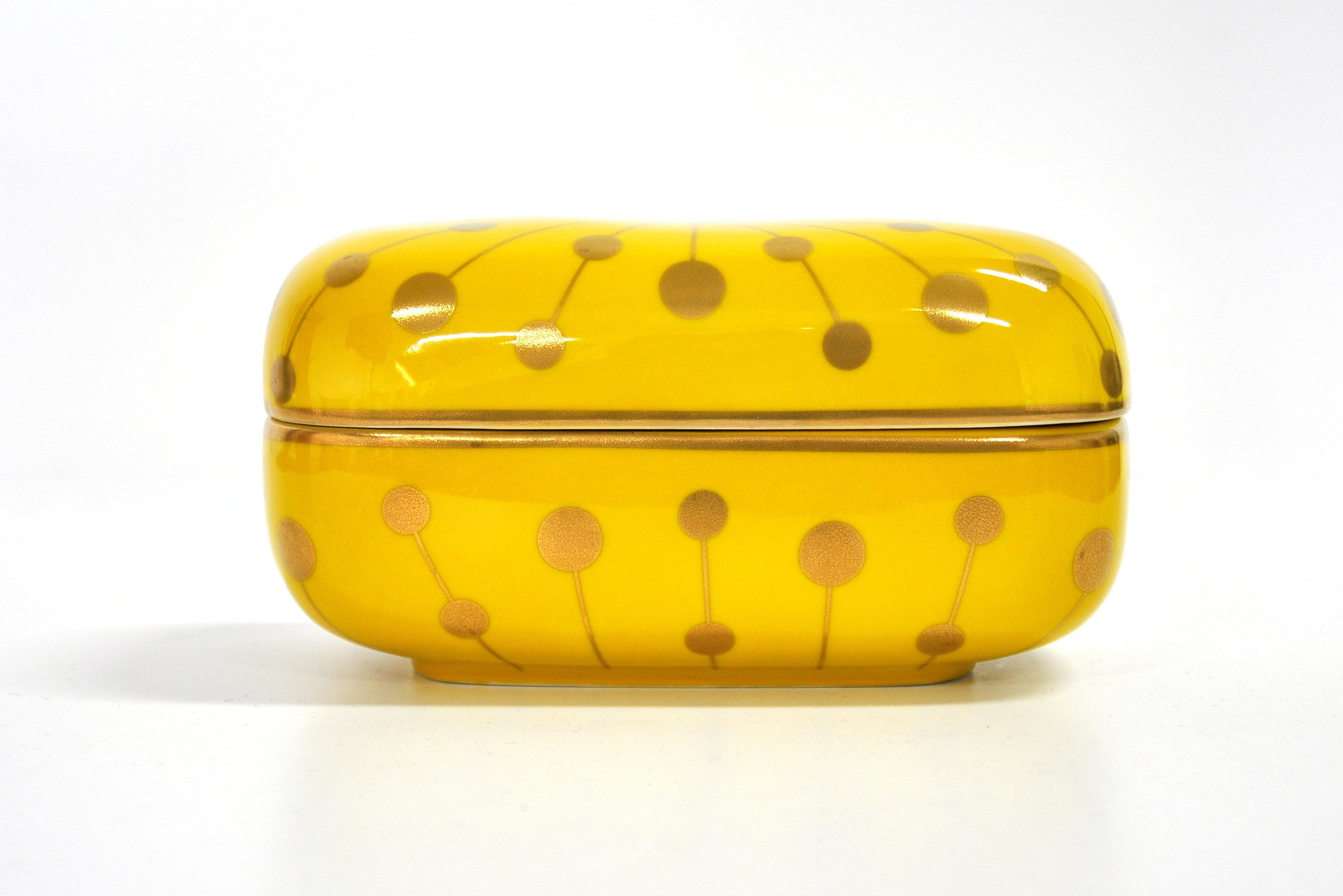 A pill shaped yellow porcelain trinket jewelry box with gold accents and white interior, by Jonathan Adler. Very decorative, makes a great gift!