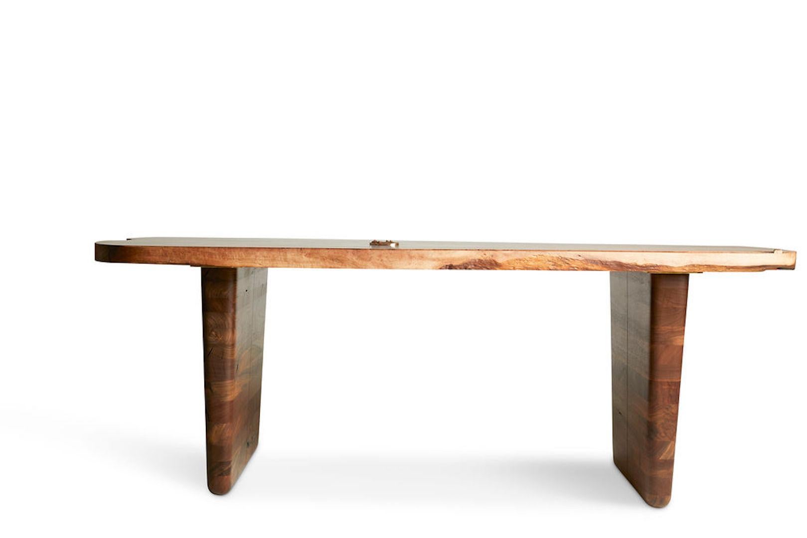 Sculptural dining table featuring a single slab claro walnut top with cast bronze inlay and bowtie. The base is made from stacked Claro, English, Bastogne, and black walnut.