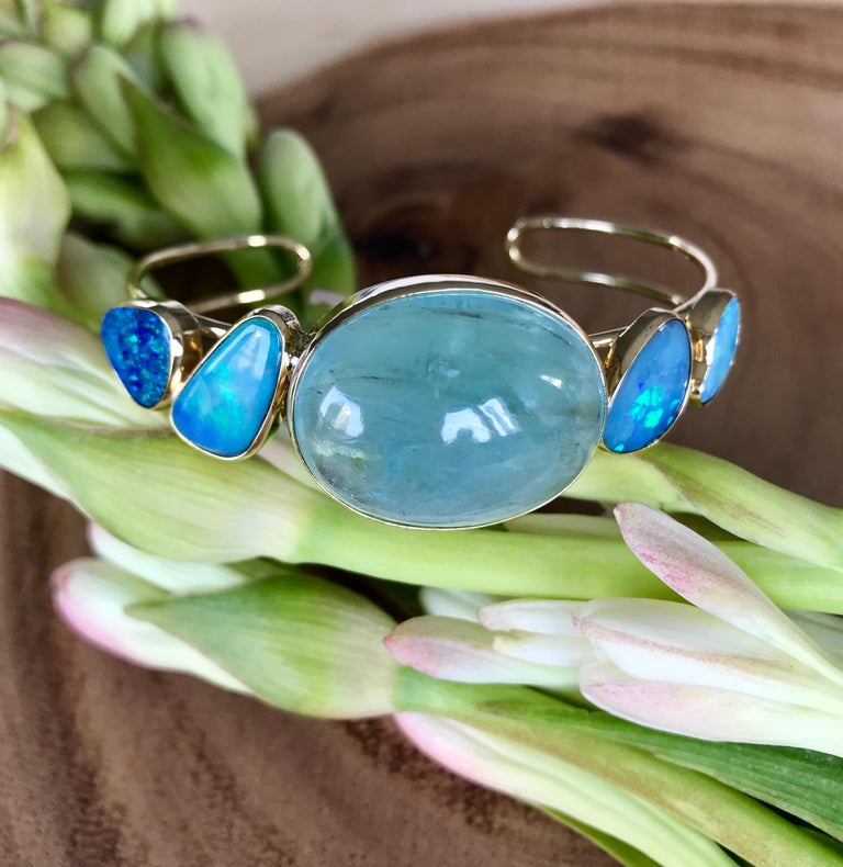 A one-of-a-kind cuff bracelet of an oval cabochon aquamarine and four boulder opals, handcrafted in 18 karat yellow gold.

This gorgeous cuff bracelet features a large luminous oval cabochon aquamarine as the center stone, flanked by two vibrant