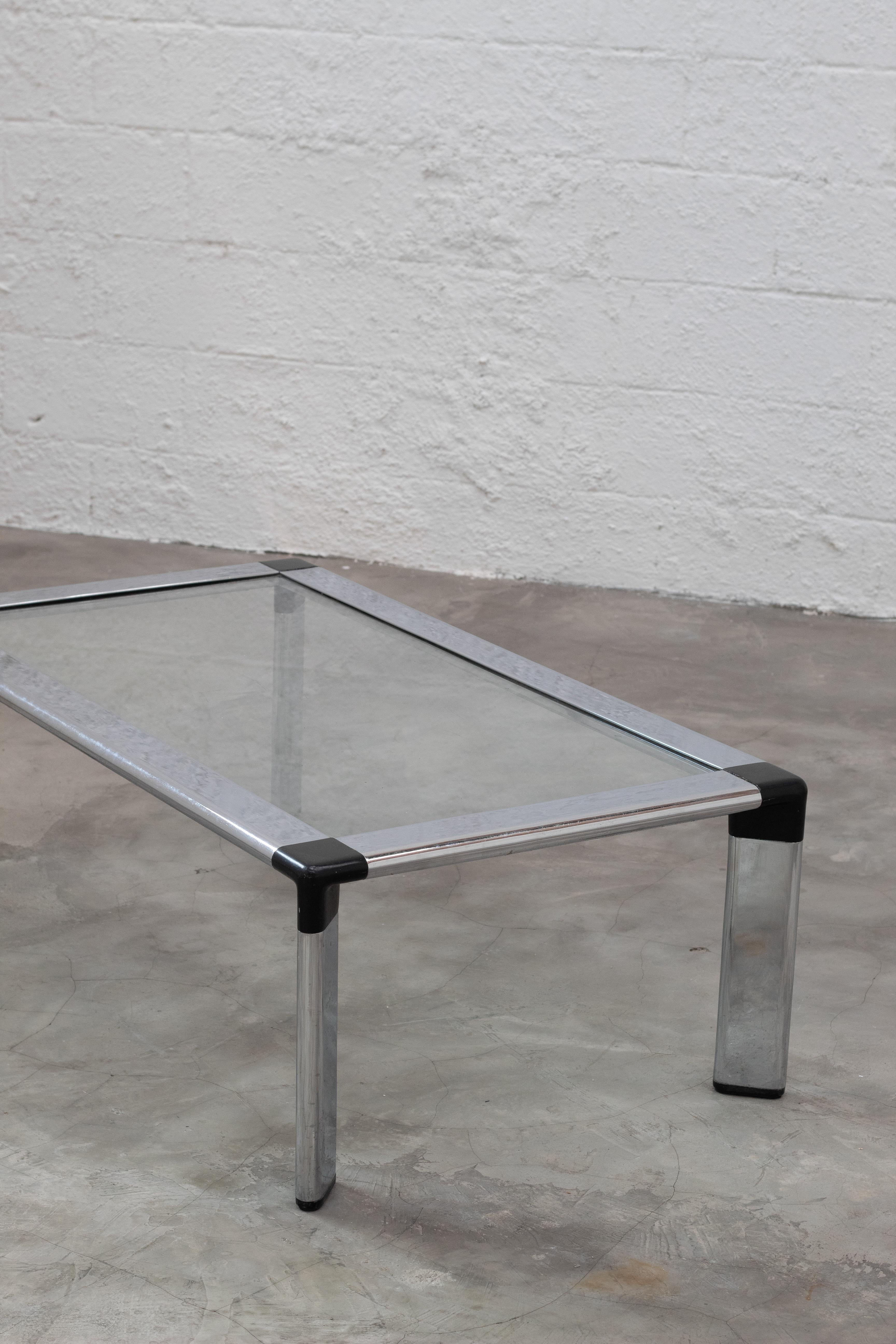 Rectangular coffee table designed by Jorge Zalszupin, featuring a sleek chrome-plated steel frame with black corner accents and a clear glass top. Its minimalist lines and refined proportions exemplify Zalszupin’s modernist approach, balancing