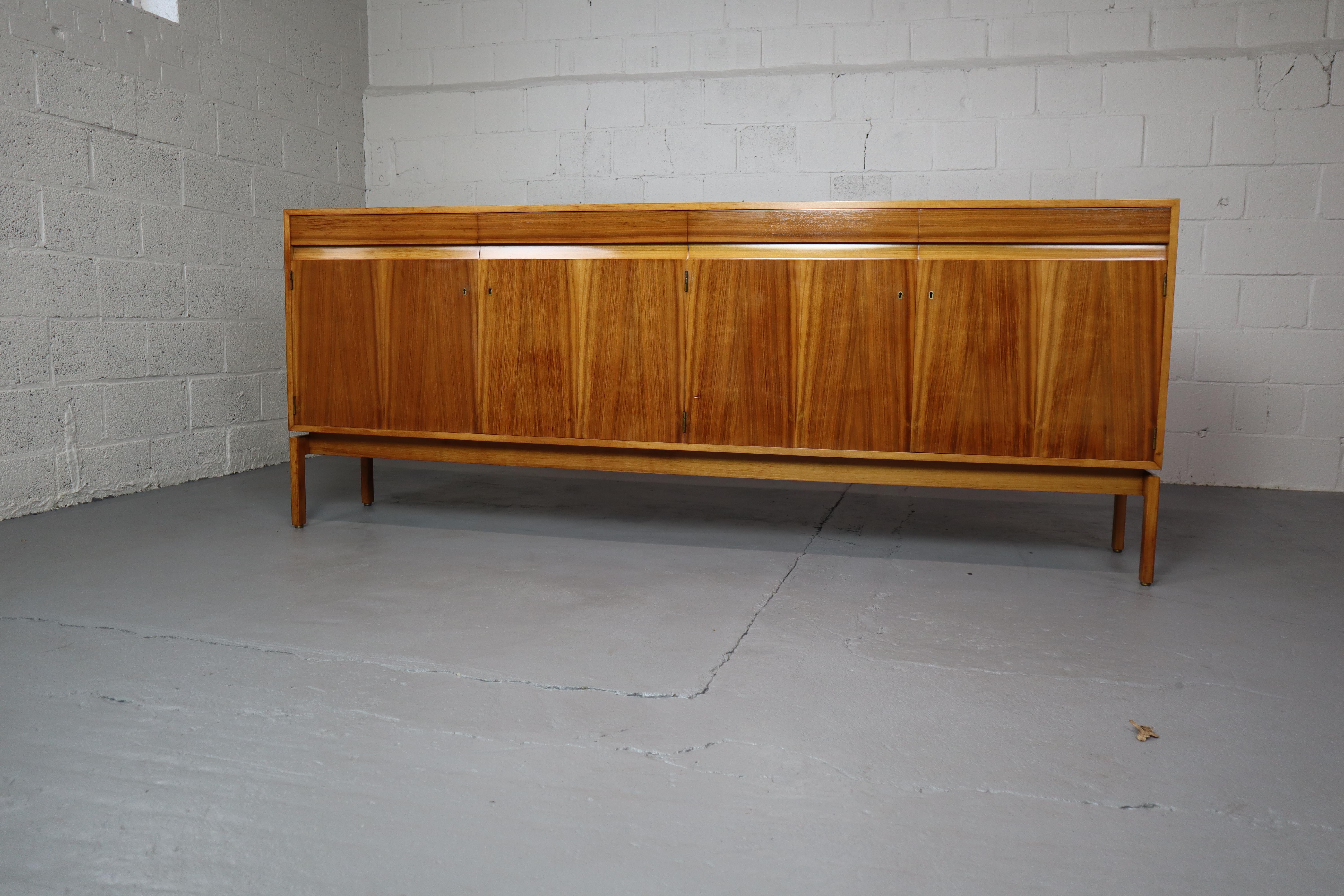 Sideboard in Walnut by Jos De Mey for Van den Berghe-Pauvers, Belgium, 1960s.  Part of the Abstracta serie. This sideboard features four large doors and four drawers. 
Each door opens and closes with a key. The cabinet has brass details and is