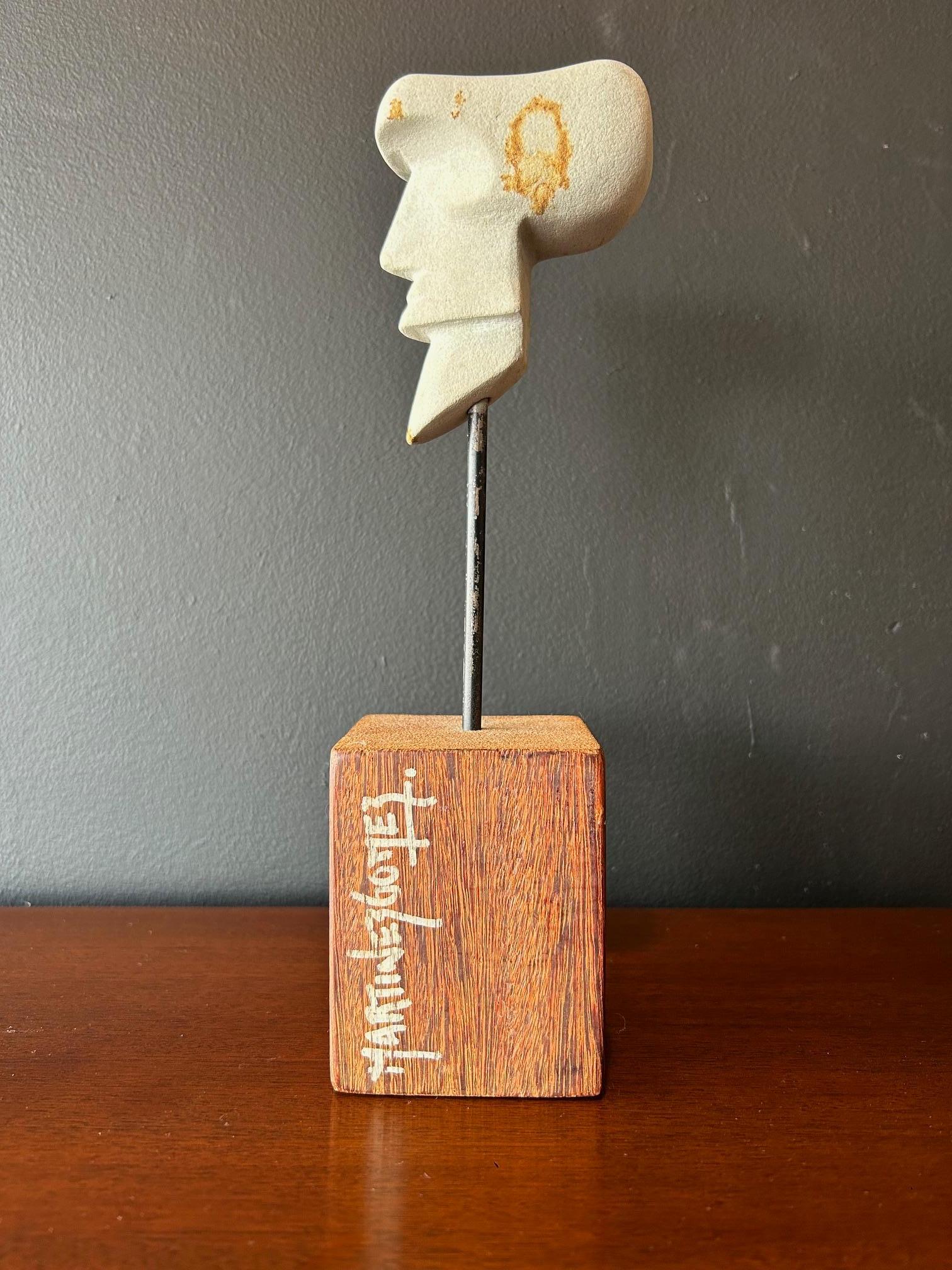 Striking, stylized carved head in white stone mounted to a wood block on an iron pole by Jose Luis Martinez Gomez (signed). 