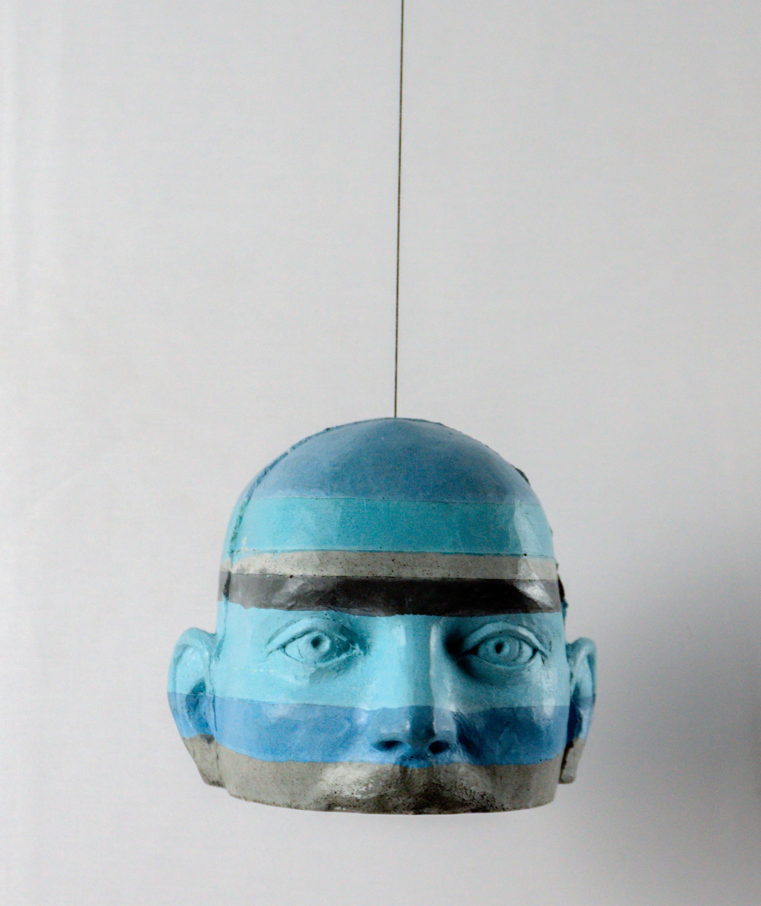 Questa scultura architettonica a testa pendente in cemento introduce un intervento cromatico distintivo all'interno della sottoserie Proyectos. Nel Progetto 21, la testa è definita da una sequenza di strisce dipinte di blu e grigio che avvolgono la