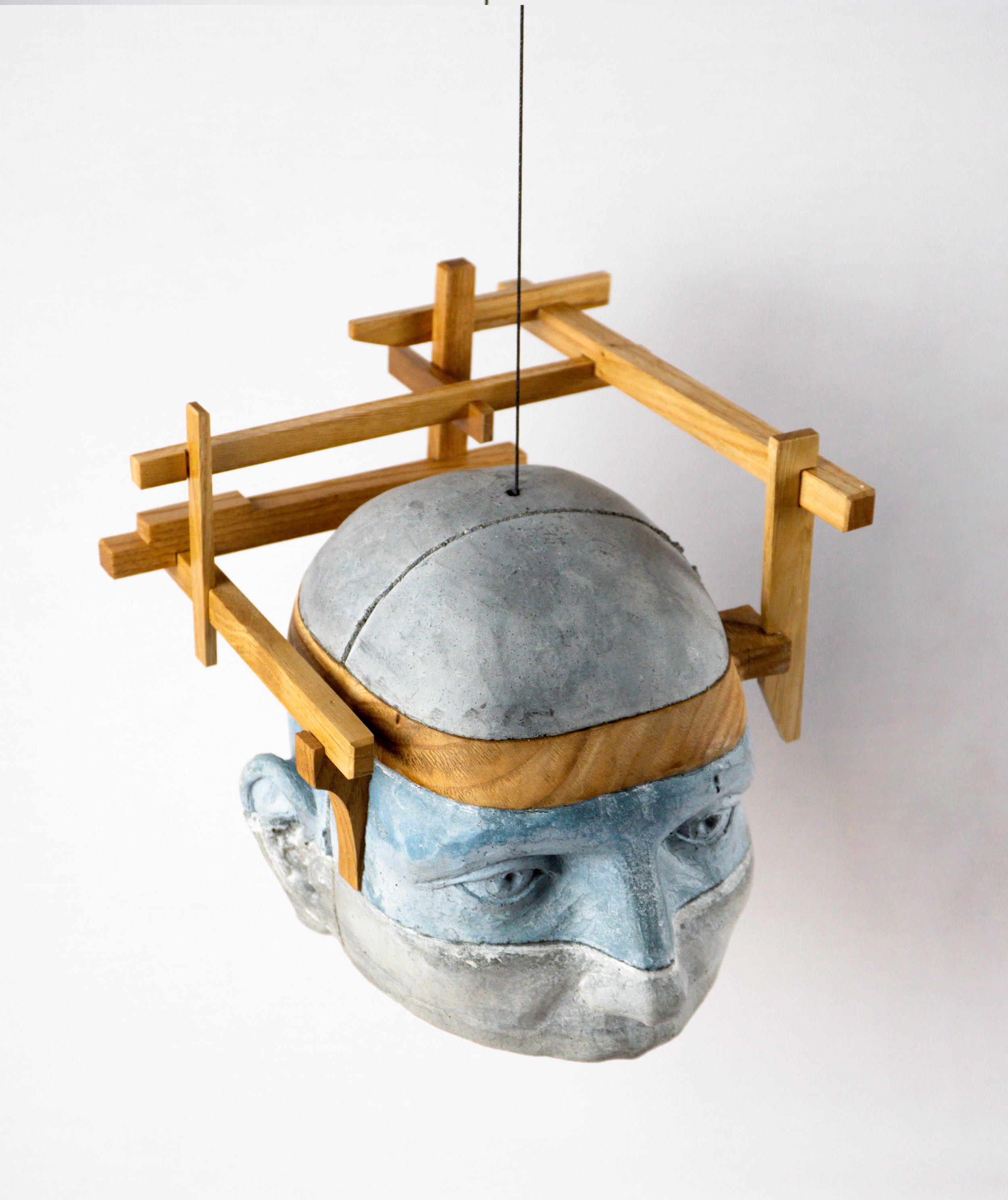 This architectural layered hanging cement head sculpture extends the conceptual language of anthropotecture by treating the human head as a suspended built structure. Project 24 introduces an external wooden framework that surrounds the upper volume