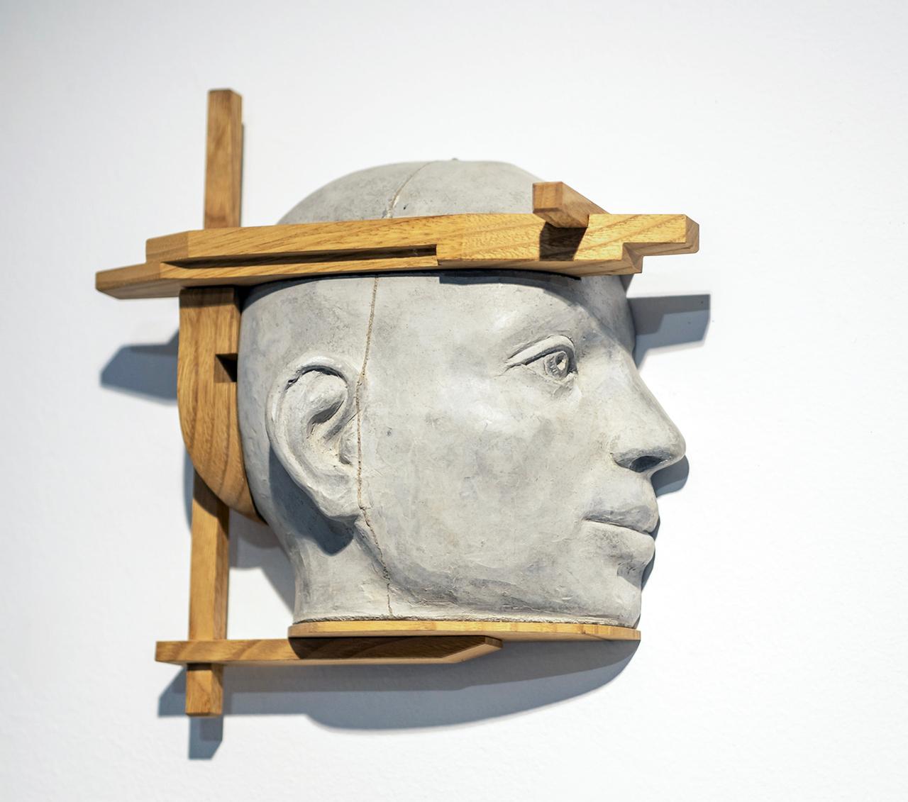 Questa scultura architettonica a parete con testa in cemento presenta una caratteristica struttura orizzontale in legno di castagno che si estende lungo i lati del viso, creando un suggestivo gioco tra ritratto e design strutturale. Nel Progetto 13,
