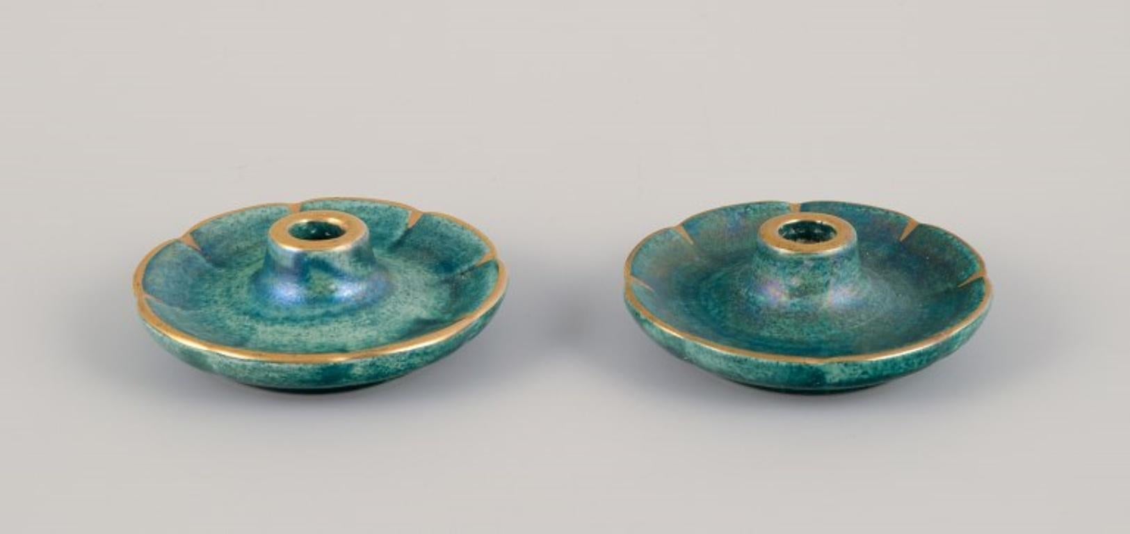 Josef Ekberg (1877-1945) for Gustavsberg, Sweden. 
Three candle holders with glaze in green-blue tones, gold decoration.
Mid-20th century.
Marked.
In perfect condition.
Tall: Diameter 9.4 cm x Height 8.5 cm.
Short: Diameter 8.0 cm x Height 3.0 cm.