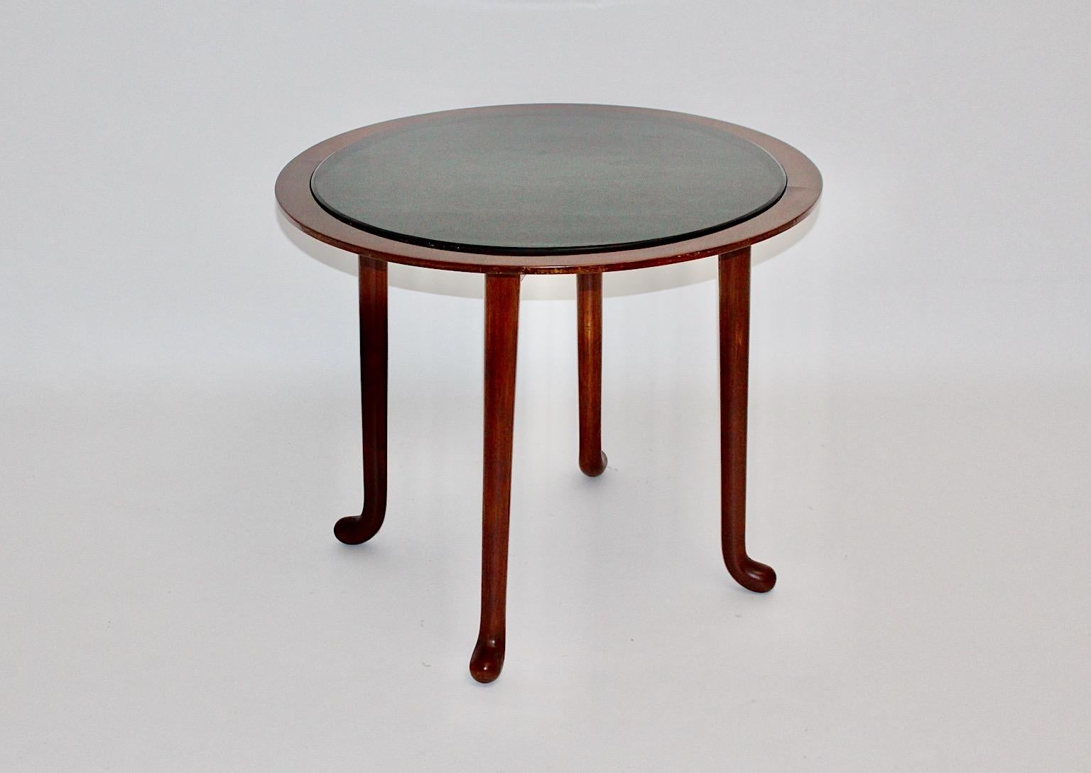 Art Deco era vintage circular side table or coffee table by Josef Frank circa 1925 Vienna from walnut veneer and solid walnut topped with an original removable black glass plate.
The authentic coffee table shows four feet with slightly curved ends