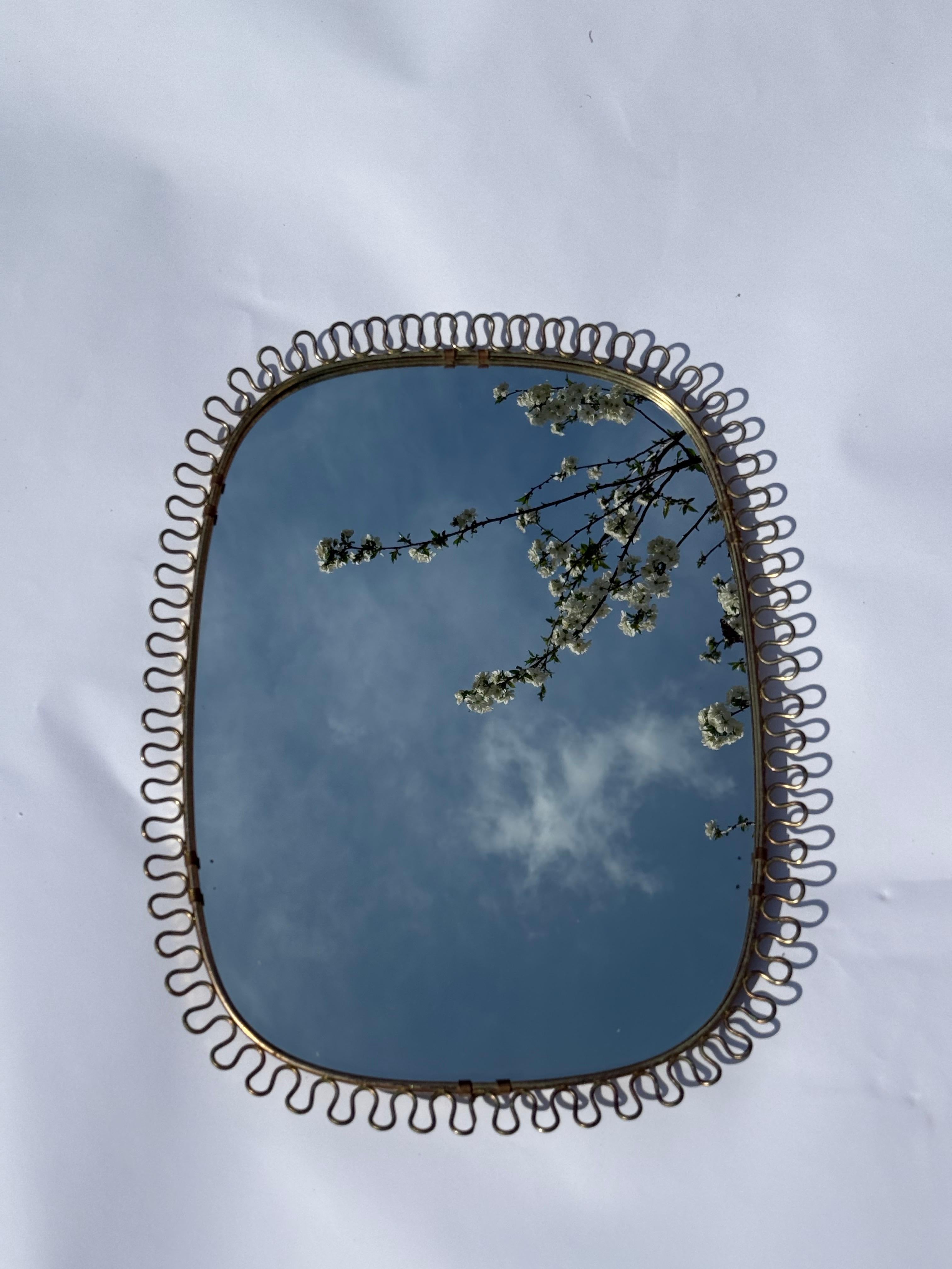 This beautiful golden filigree wall mirror is made of brass in a loop design from the 50s. The back of this mirror is made of wood which makes it extremely stable and beautiful. The mirror glass is still in a good and beautiful clear condition.  The