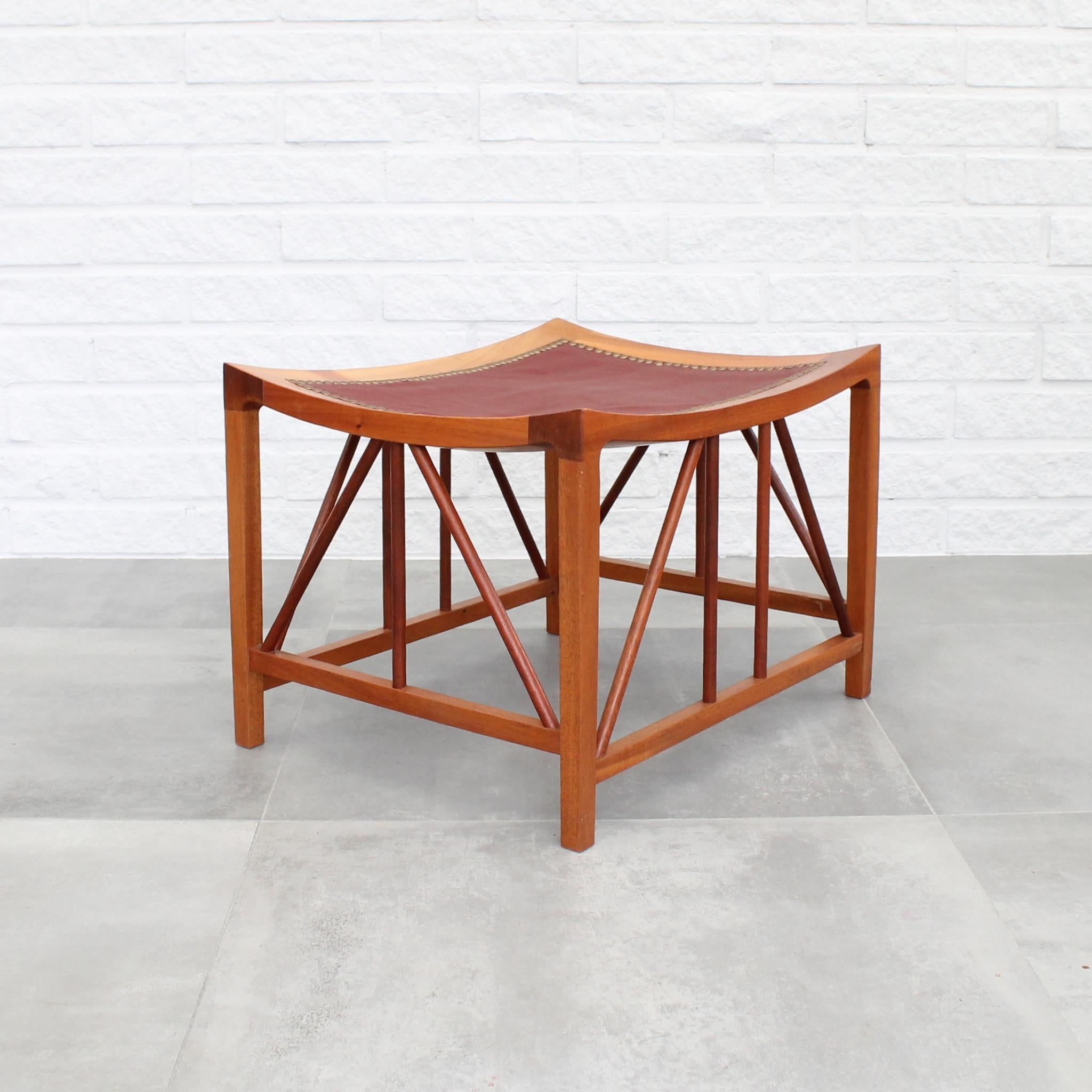 Stool model 1063, designed by Josef Frank for Firma Svenskt Tenn. Crafted from solid walnut and adorned with red leather upholstery, it features decorative brass rivets encircling the seat. Josef Frank drew inspiration from an ancient source for