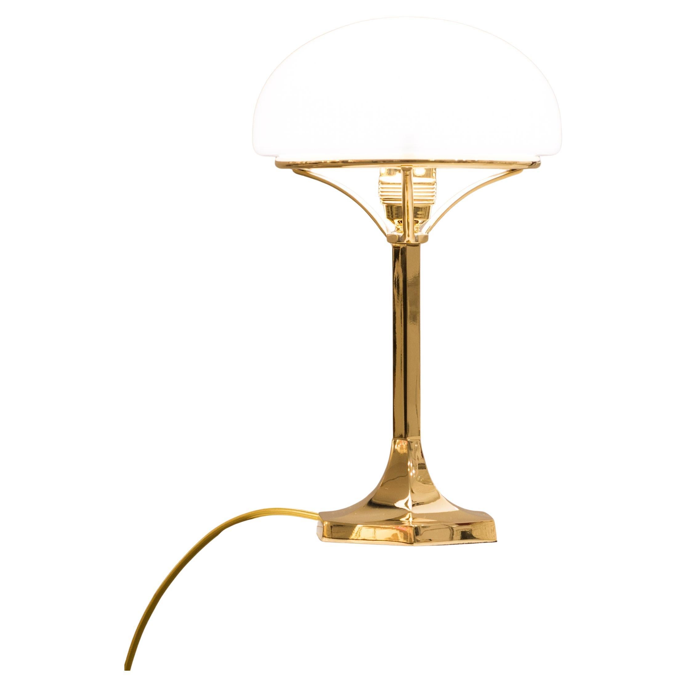 Una lampada da tavolo con paralume in vetro opalino, in ottone.
Ottone, opzionalmente verniciato o nichelato, tutte le altre superfici su richiesta, vetro opalino, soffiato a mano.

La maggior parte dei componenti è conforme alle norme UL; con un