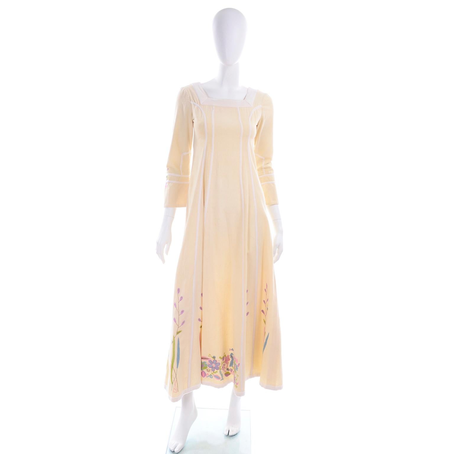 Dies ist ein cremefarbenes, schweres Baumwollkleid mit handgestickten Blumen und Vögeln in den Farben rosa, lila, blau, lindgrün und hellbraun. Dieses nicht etikettierte Josefa-Kleid hat eine mit weißem Samt eingenähte Bandverzierung entlang der